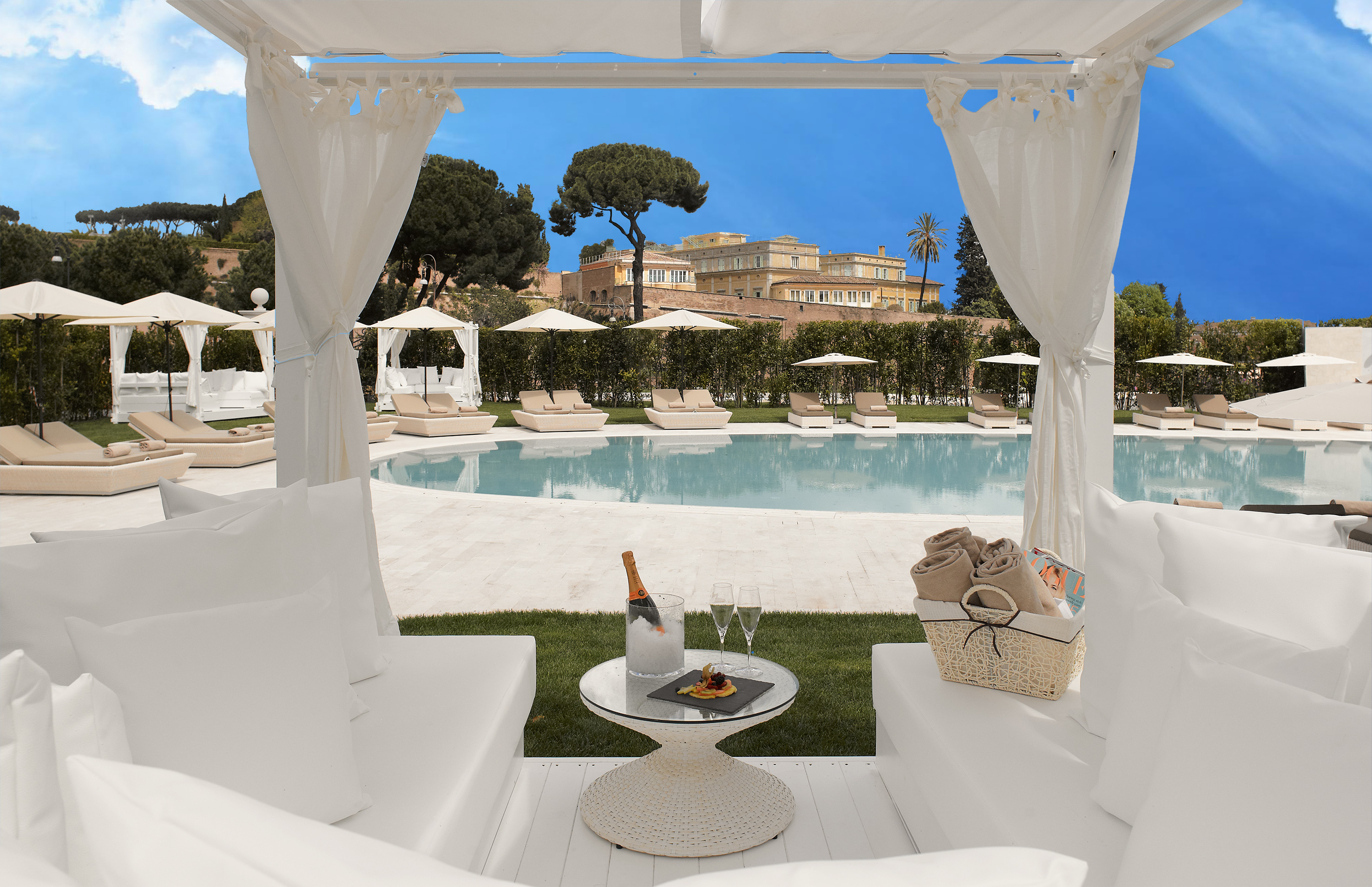 White luxury cabana, champagne by resort pool, historic Rome backdrop.