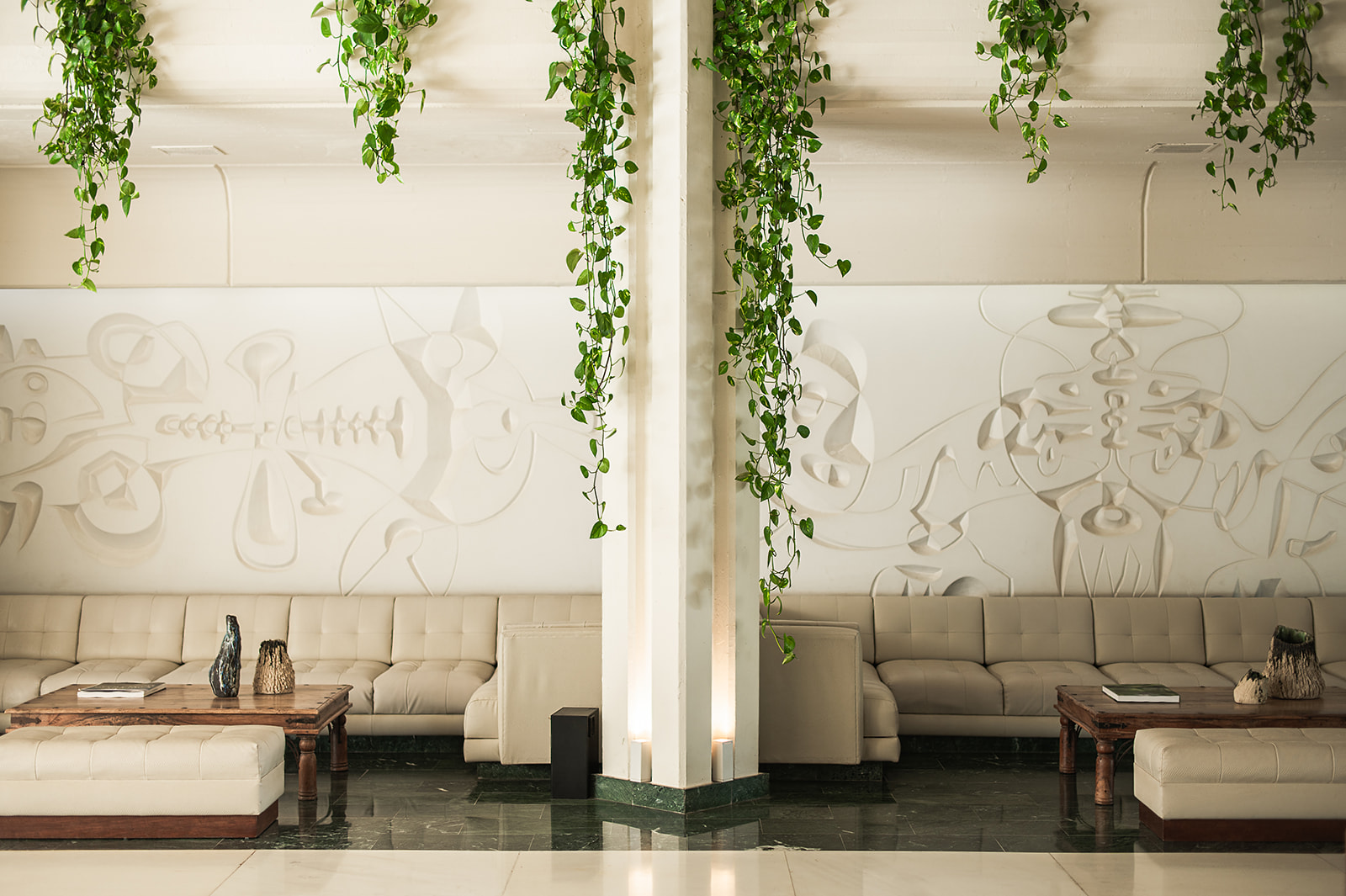 Modern lobby with abstract wall art, cream sofas, and hanging green vines.
