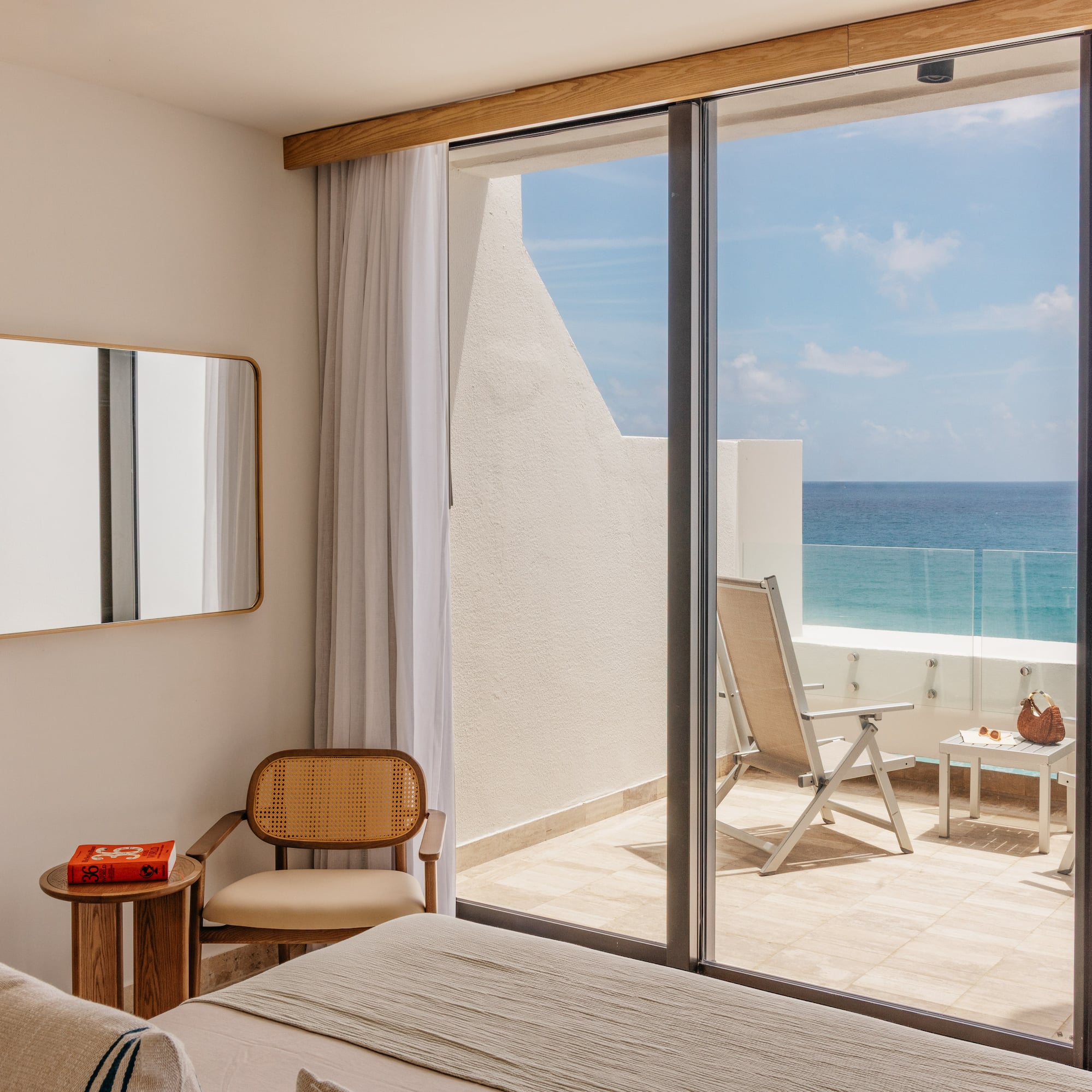 Ocean view bedroom with modern decor, balcony, and lounge chairs.