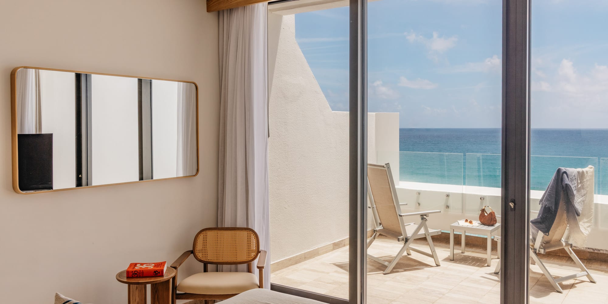 Ocean view bedroom with modern decor, balcony, and lounge chairs.