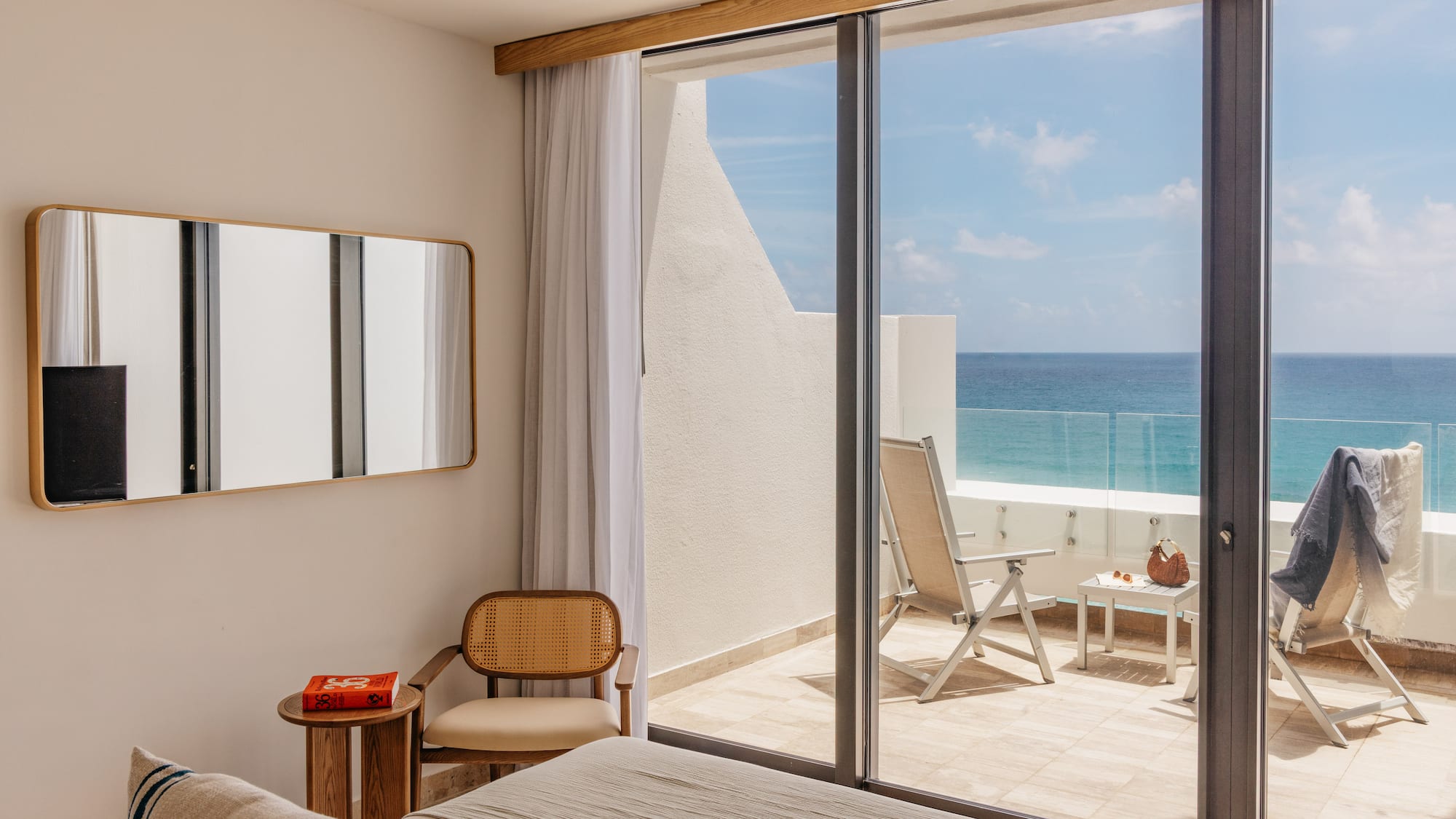 Ocean view bedroom with modern decor, balcony, and lounge chairs.