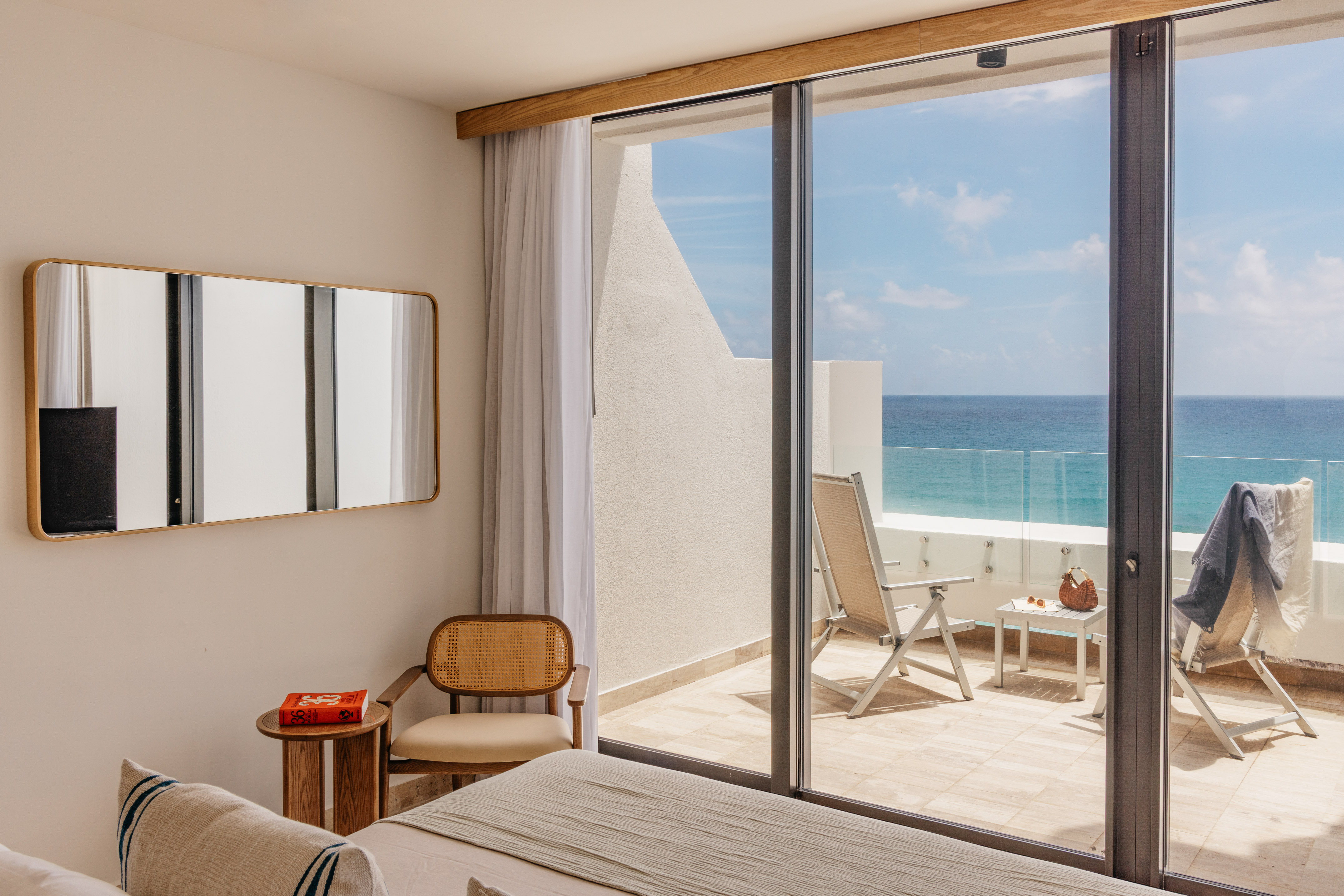 Ocean view bedroom with modern decor, balcony, and lounge chairs.