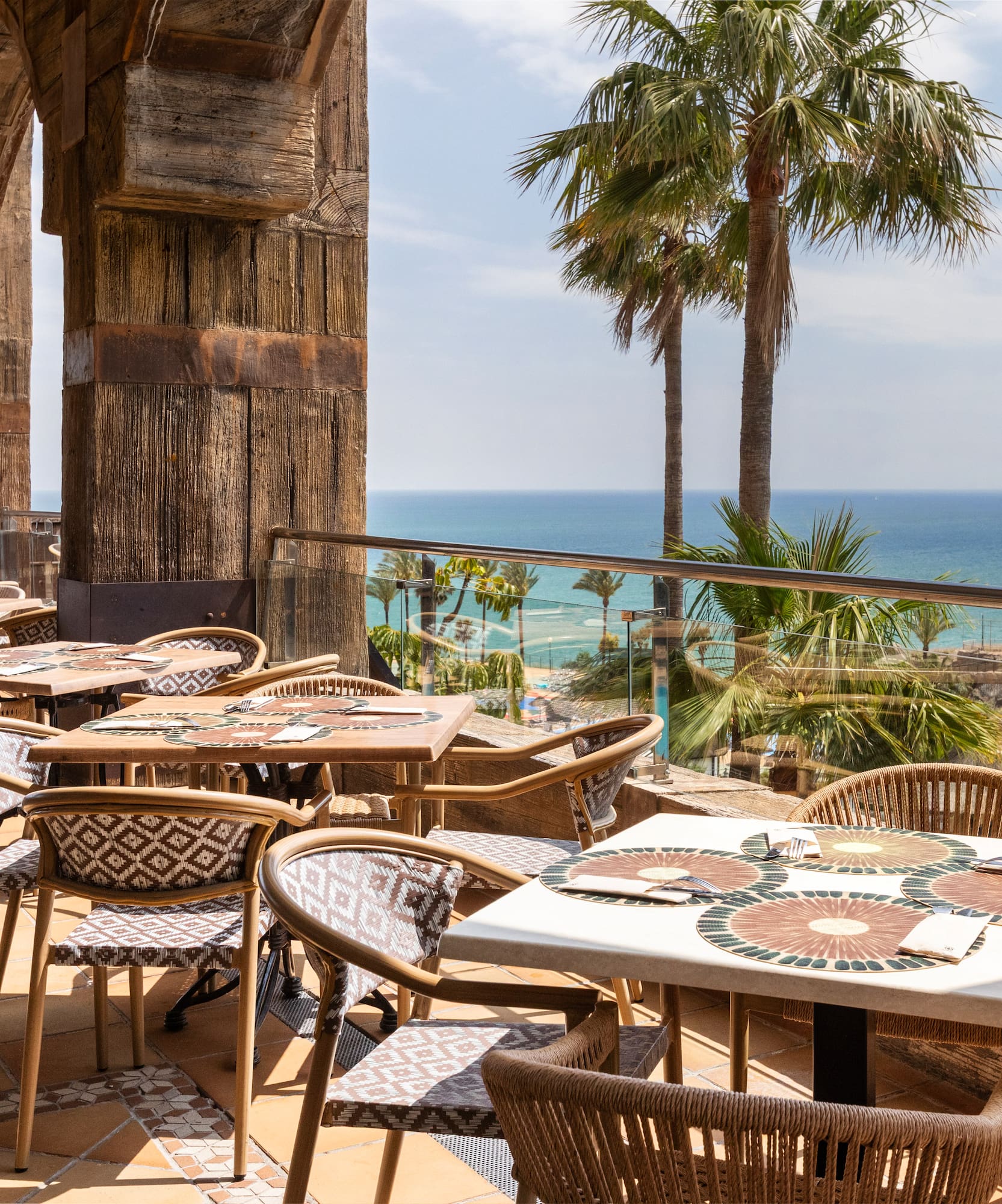 Outdoor ocean view restaurant terrace with palm trees and a distant lighthouse.