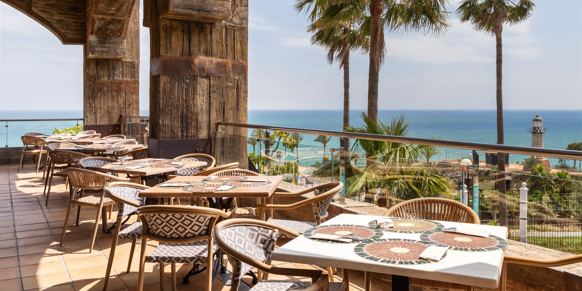 Beachfront dining terrace with sea view, palm trees, and a lighthouse.
