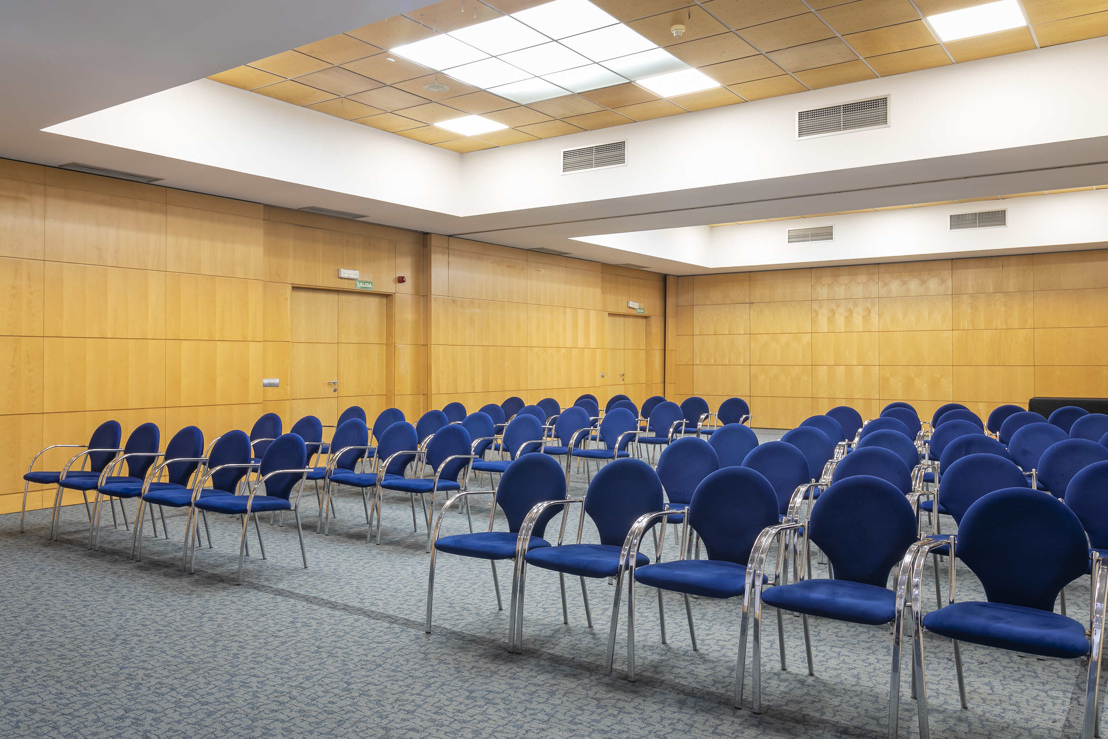 Spacious conference room with blue chairs, wood paneling, and bright lighting.