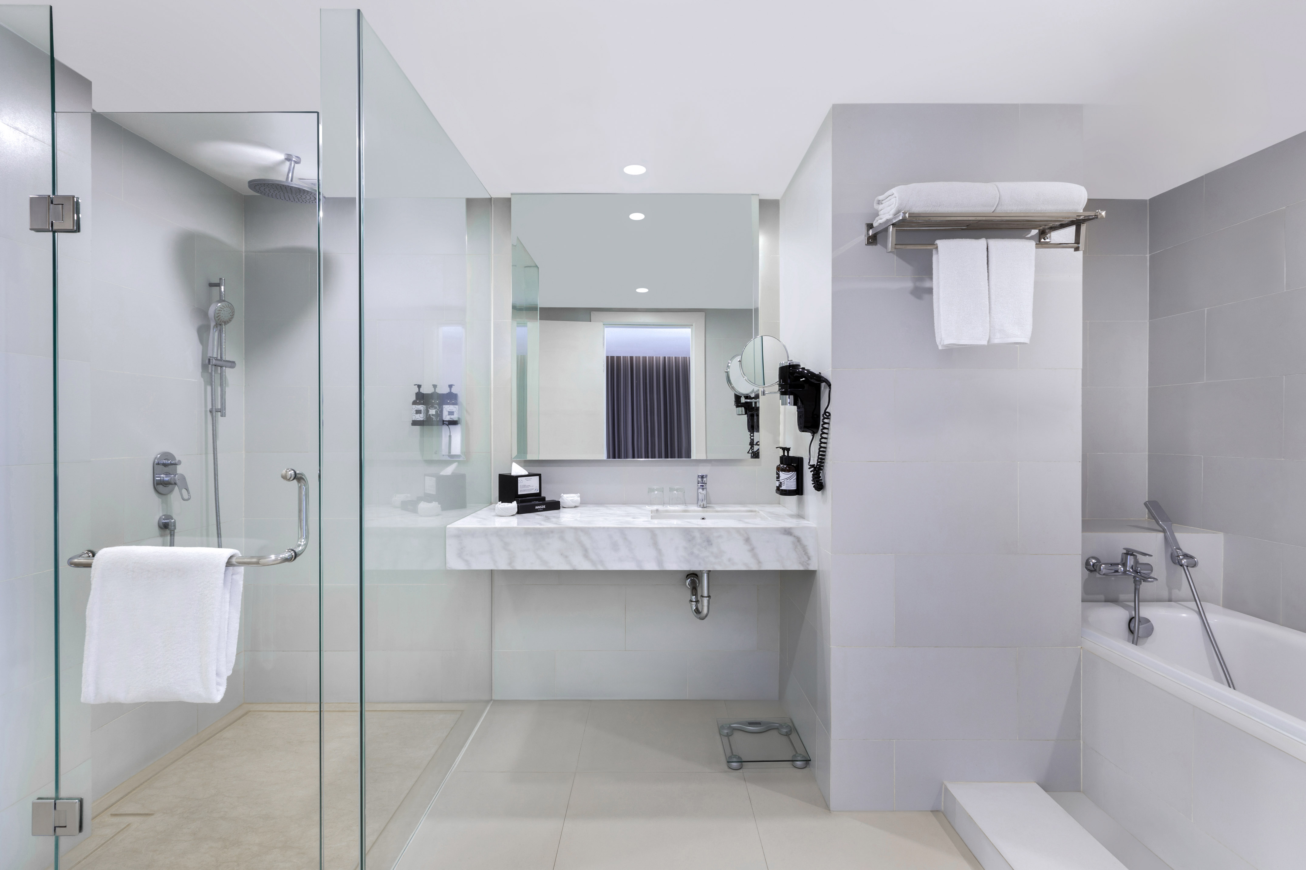 Modern hotel bathroom with glass shower, bathtub, marble vanity, and mirror.