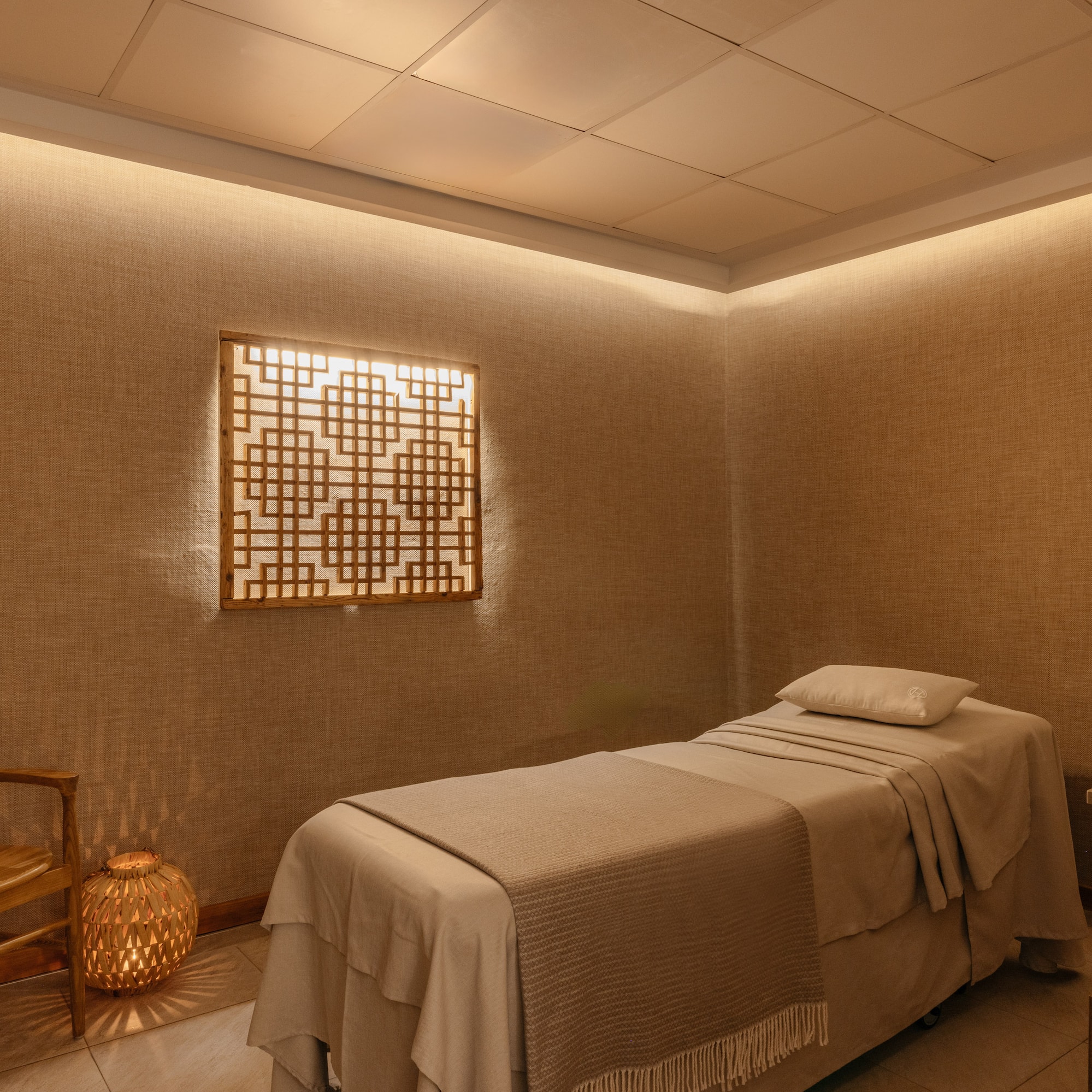 Serene spa room with massage bed, wooden chair, and warm ambient lighting.
