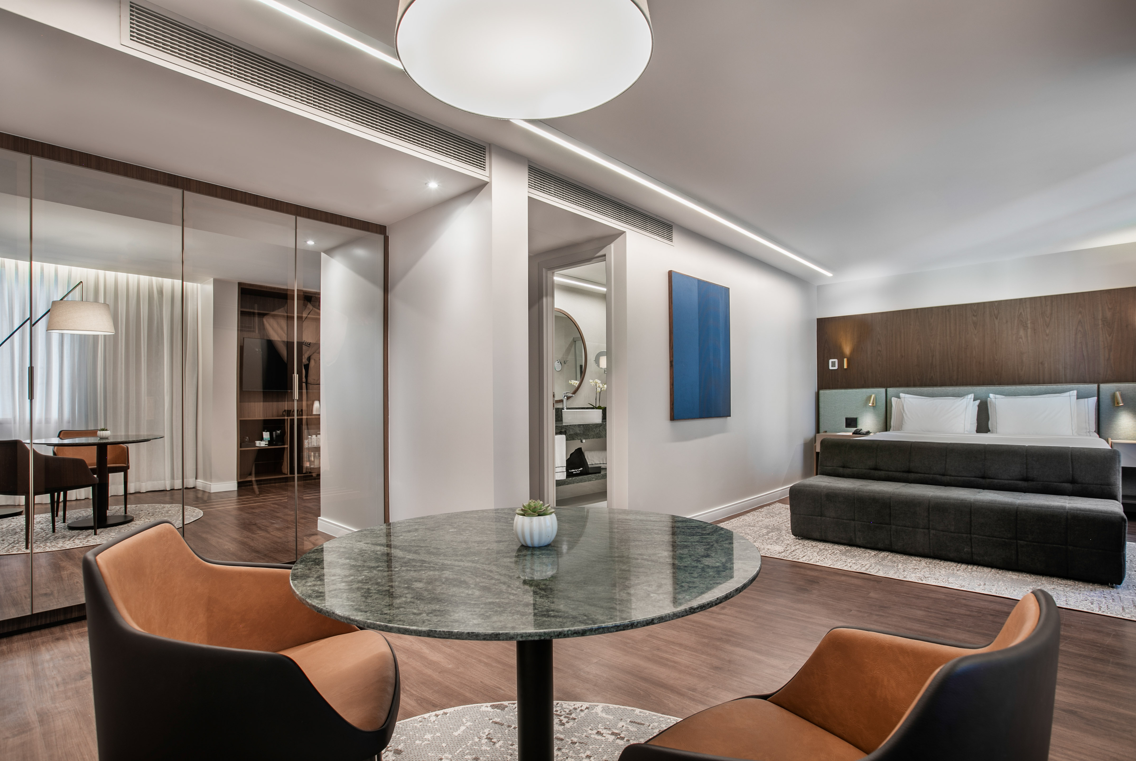 Modern luxury hotel suite with bedroom, marble table, and sitting area.