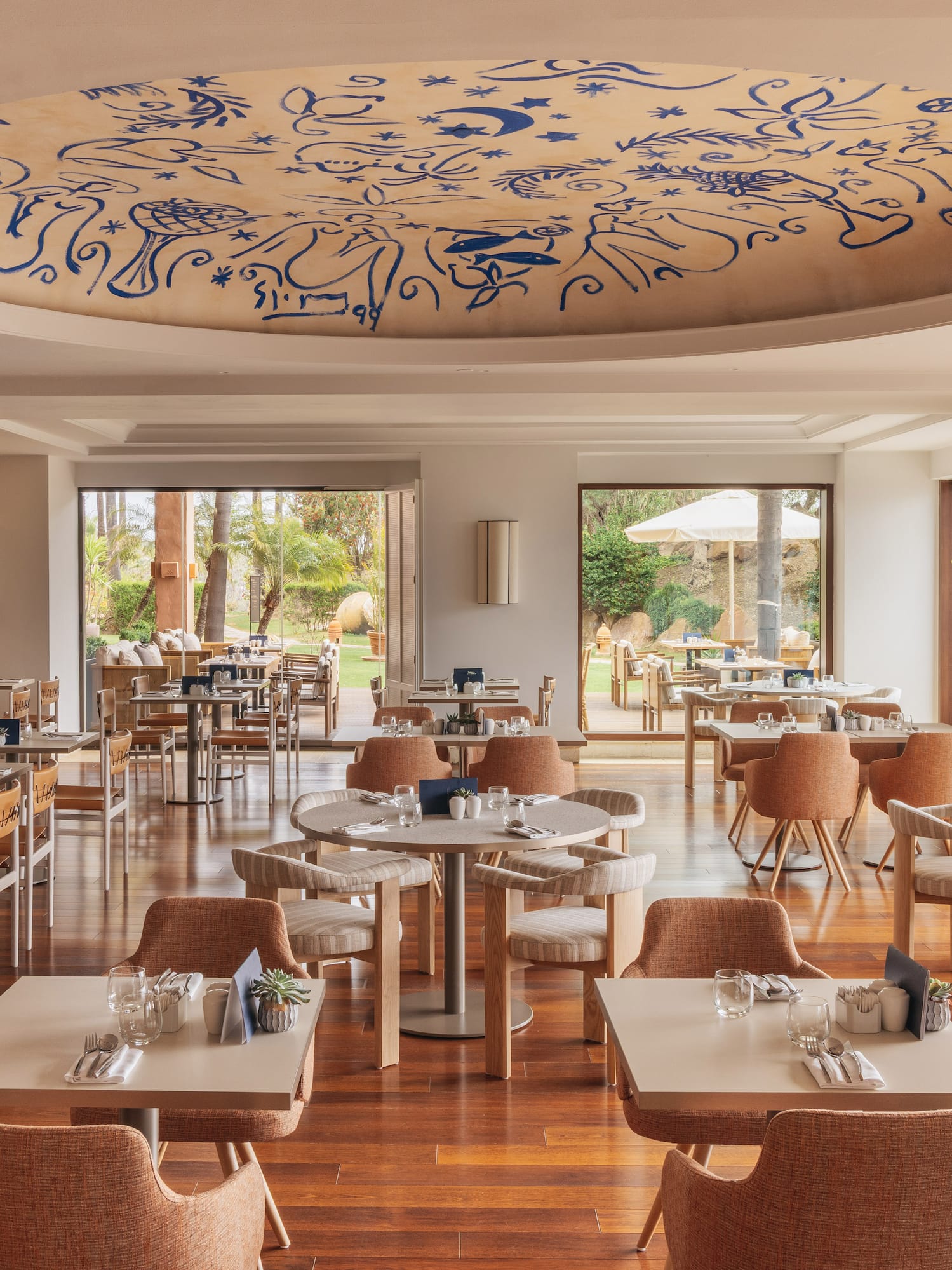 Spacious restaurant with blue ceiling mural, wooden floors, and garden views.
