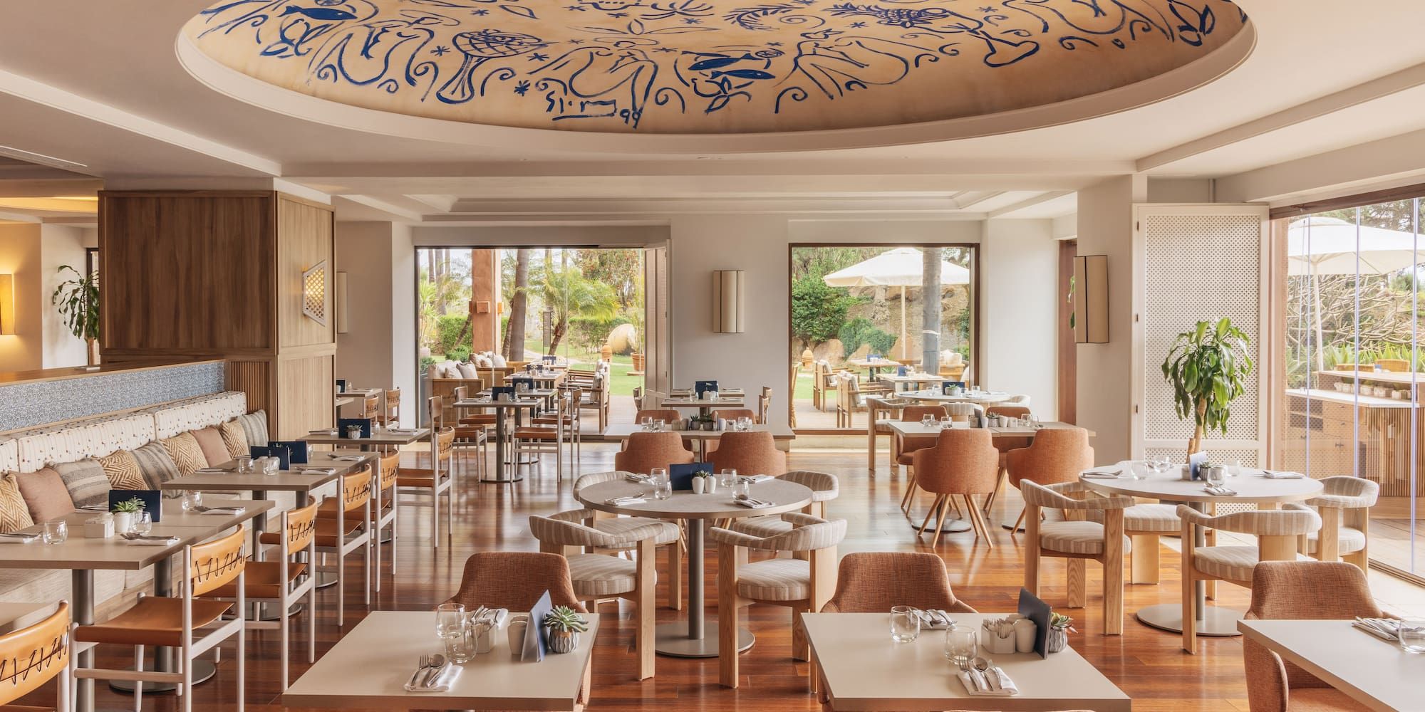 Modern restaurant dining room, blue patterned ceiling, wood floor, garden view.