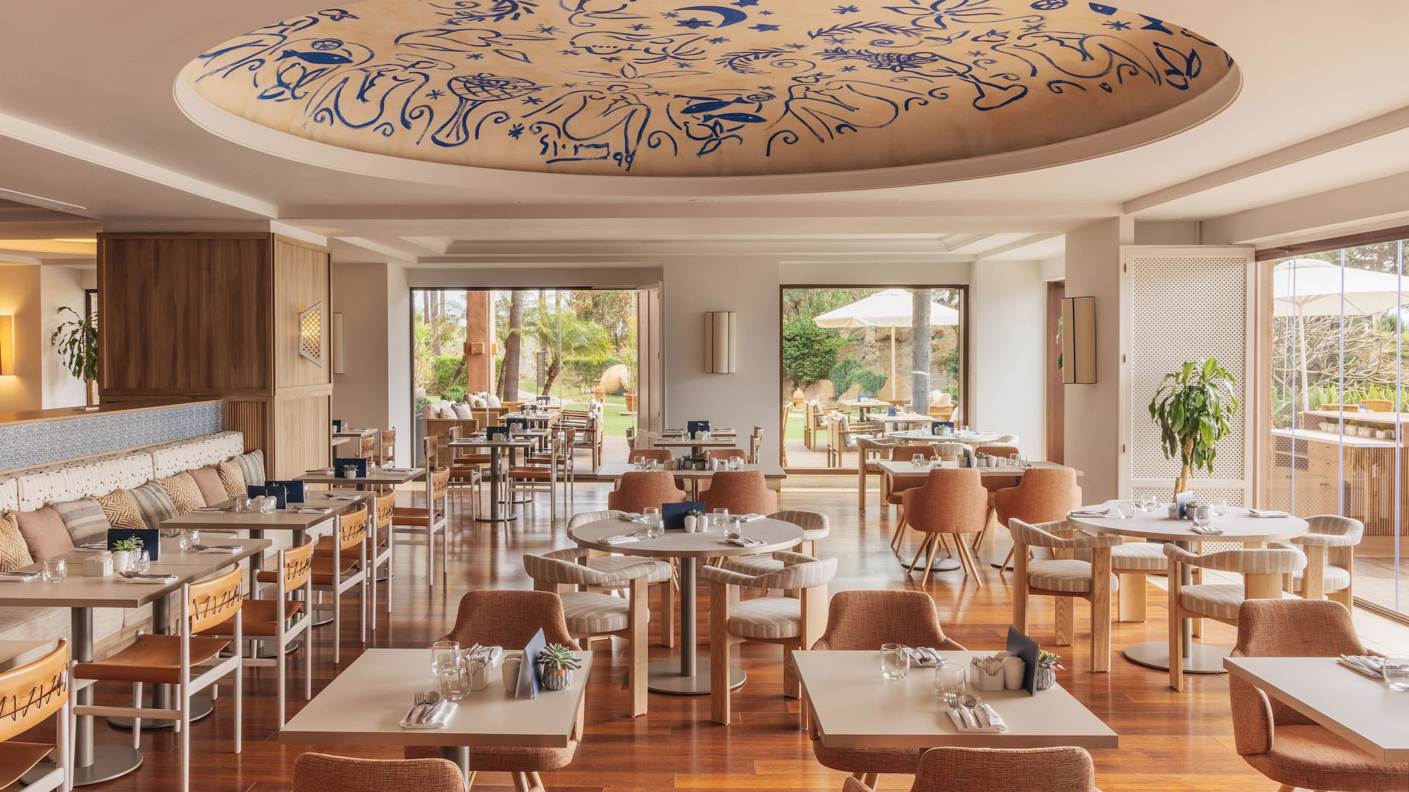 Modern restaurant dining room, blue patterned ceiling, wood floor, garden view.