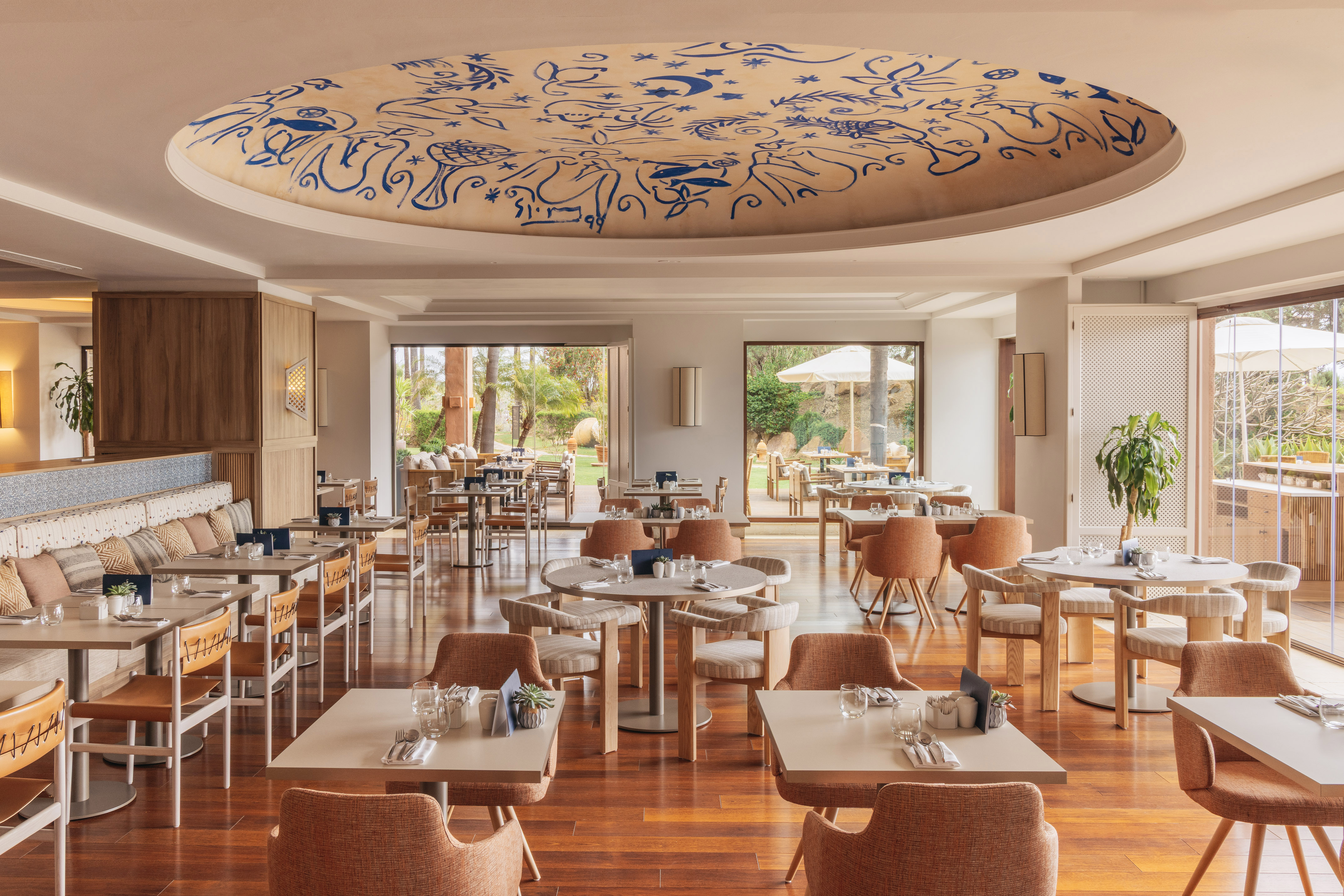 Modern restaurant dining room, blue patterned ceiling, wood floor, garden view.
