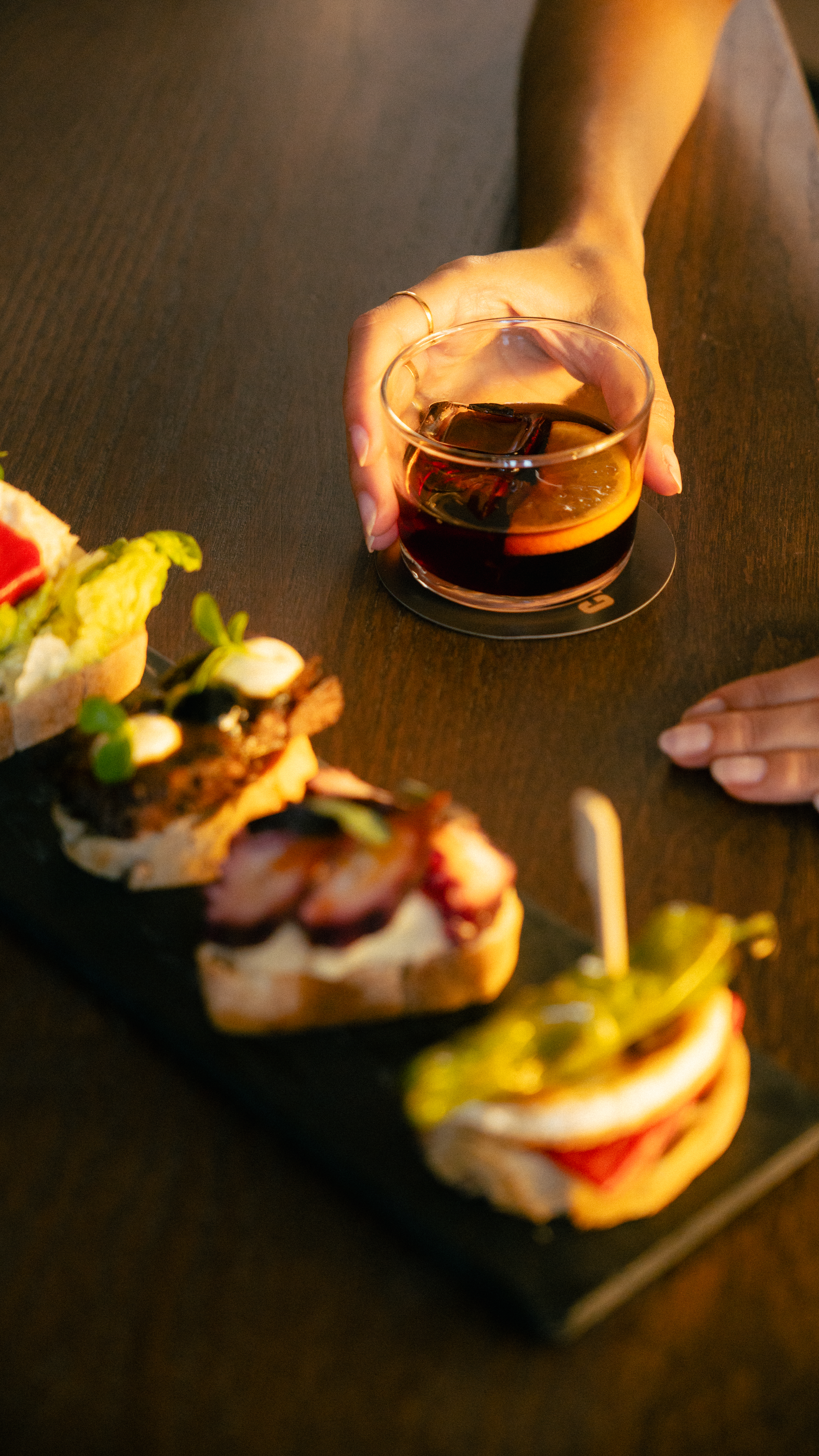 Hand with cocktail, alongside a platter of Spanish pintxos and tapas.