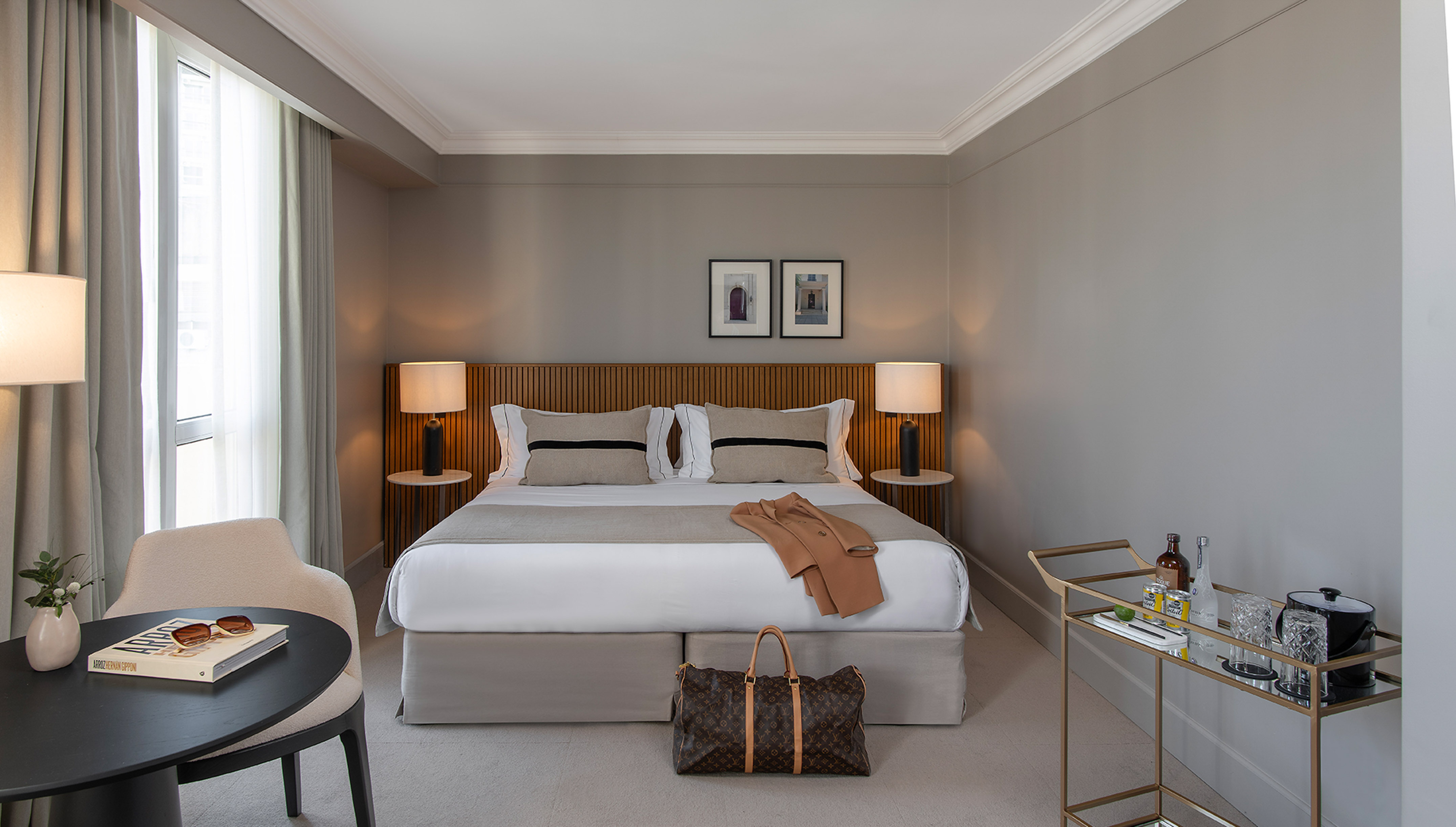 Elegant hotel bedroom with king bed, modern design, luggage, and minibar cart.