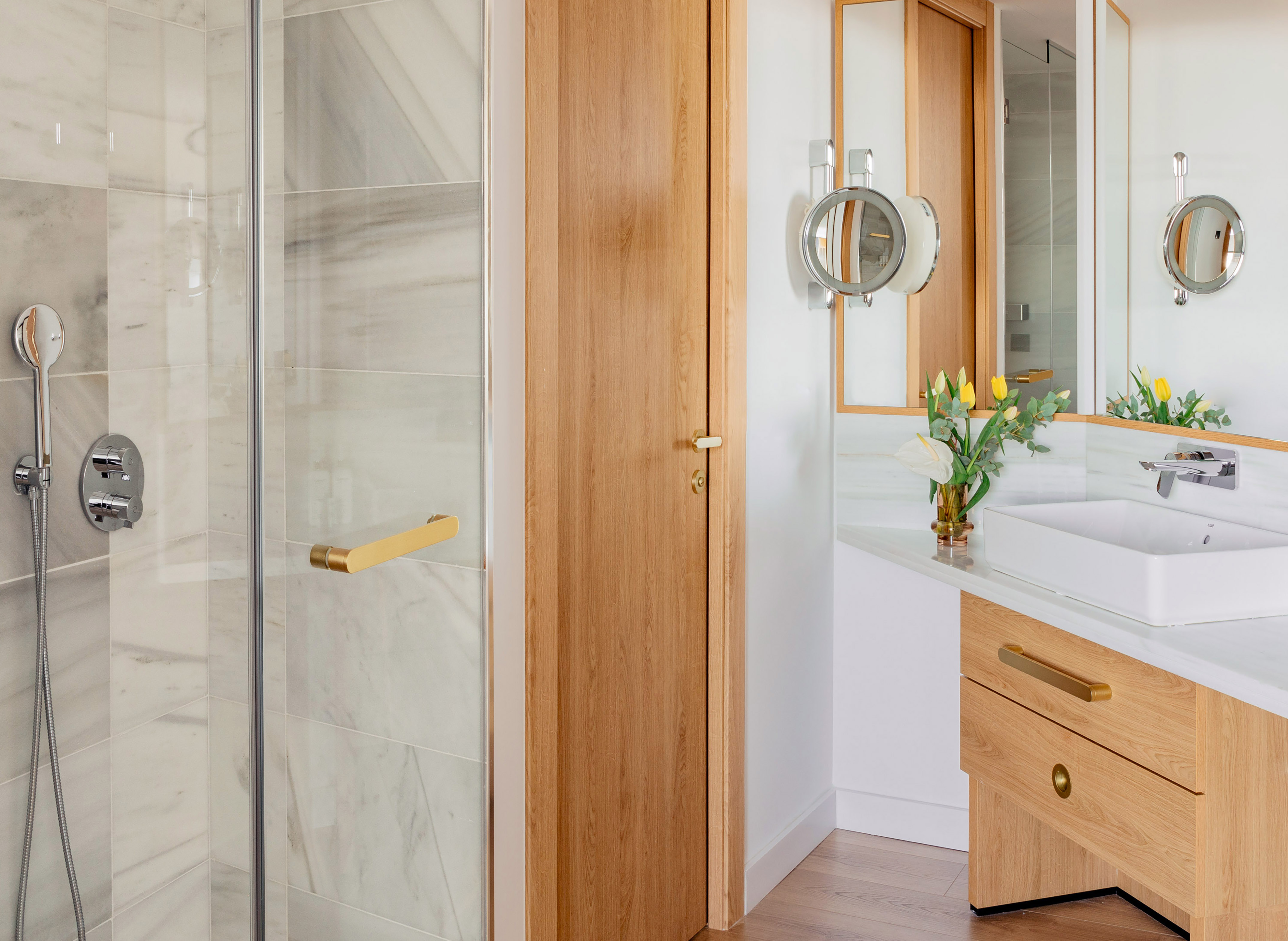 Modern bathroom with marble shower, wooden vanity, and brass accents.