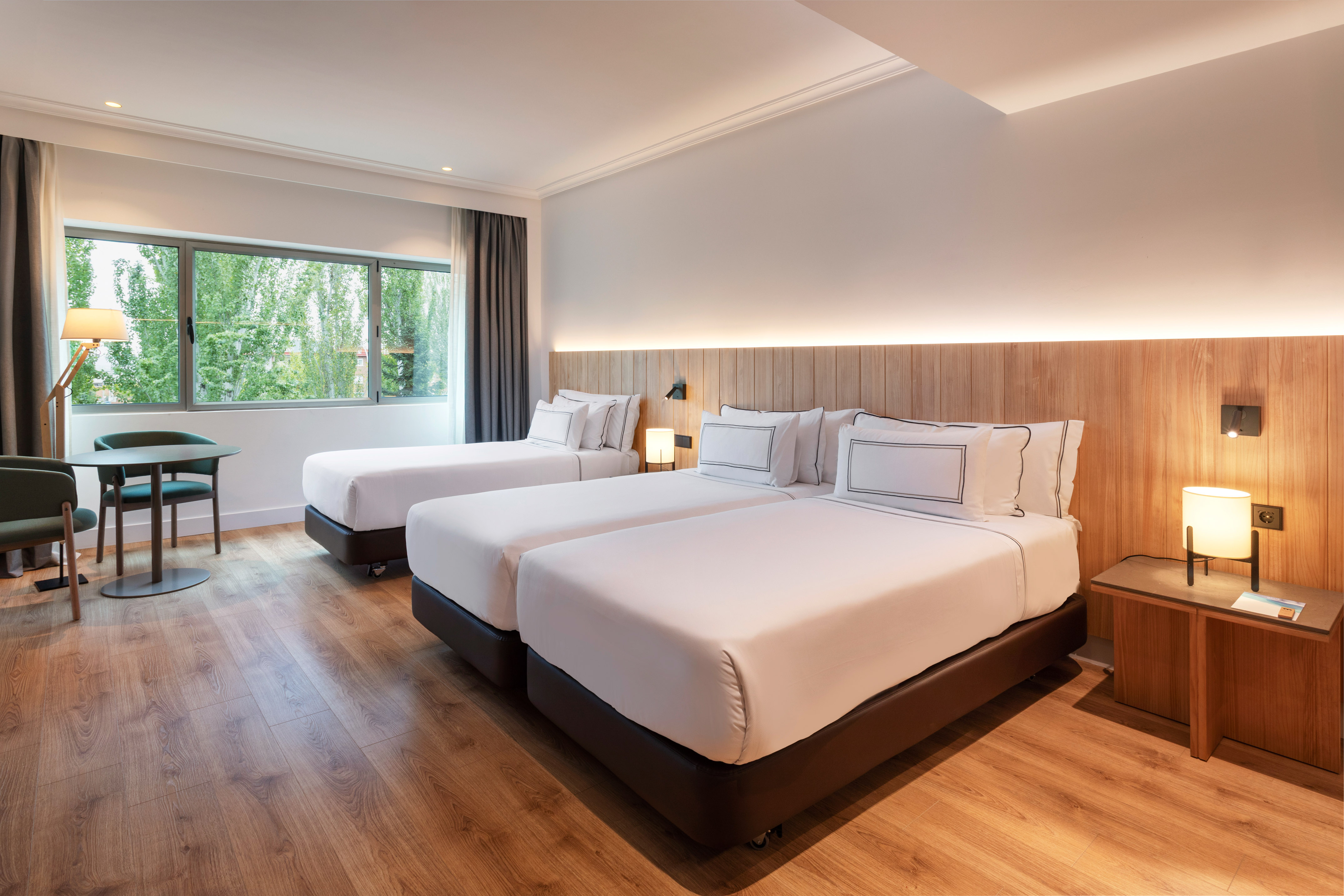 Modern hotel room with two twin beds, wooden floor, and large window view.