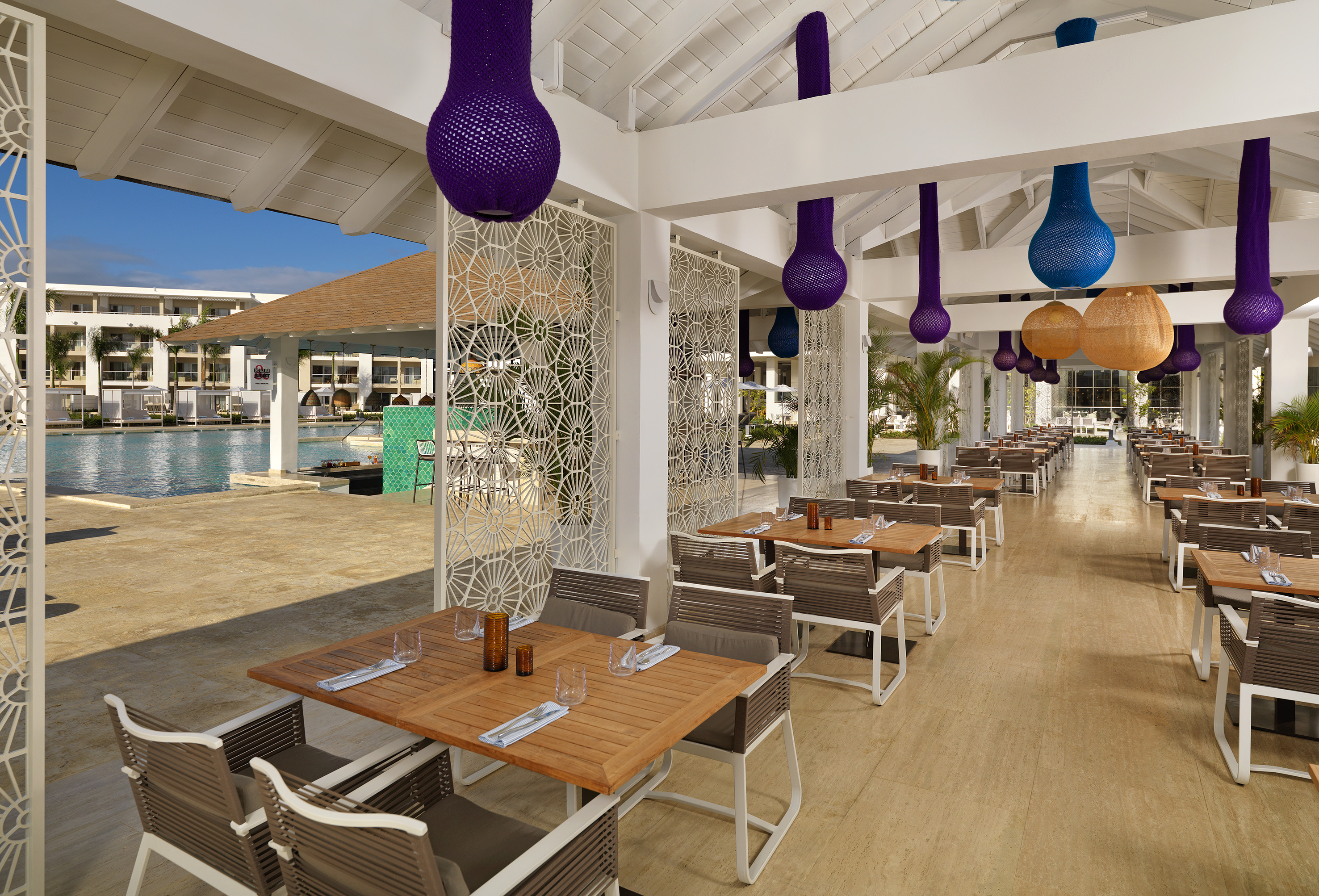 Outdoor resort dining with colorful hanging lamps and poolside views.
