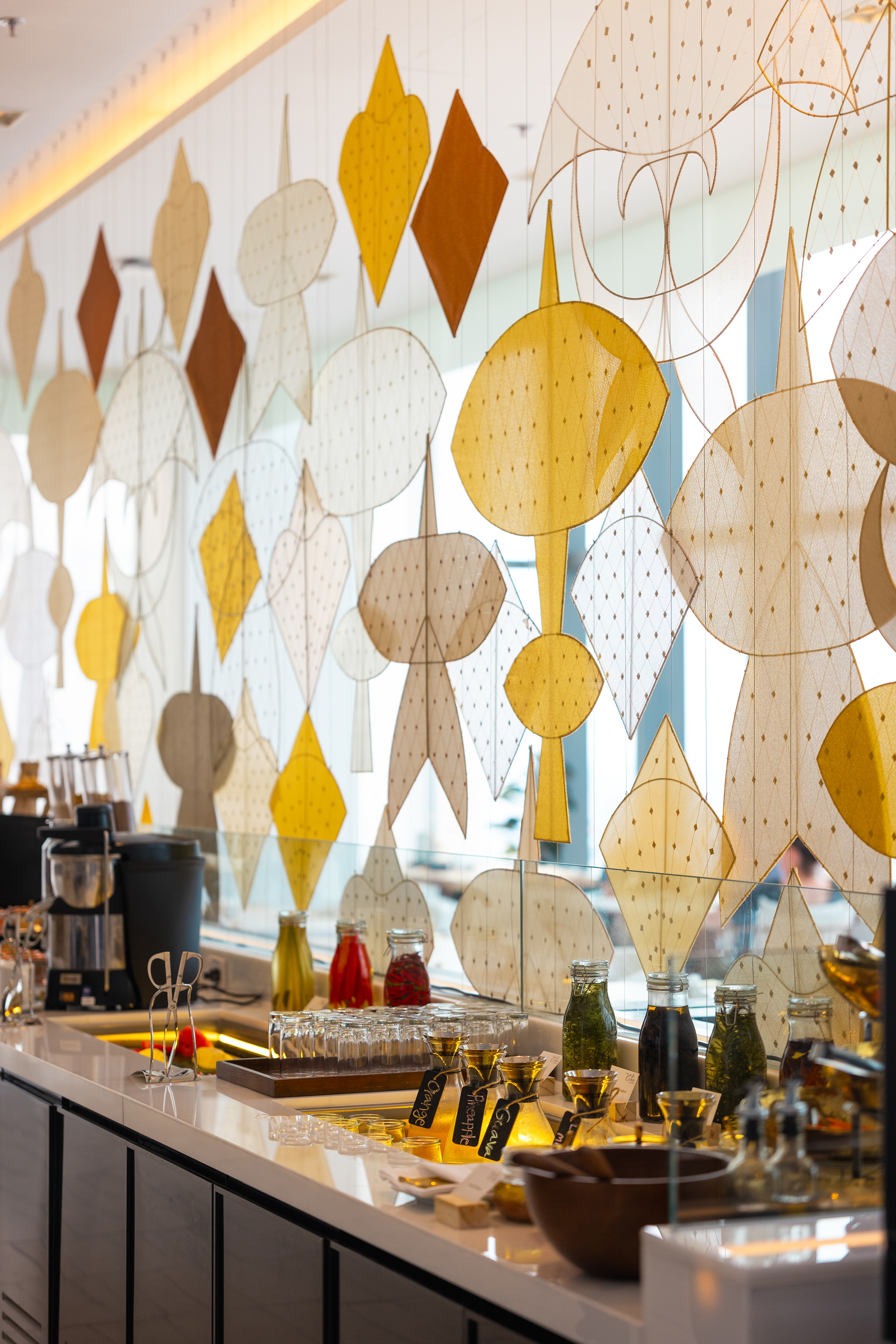 Decorative fabric kites behind a modern buffet counter with juices and coffee.