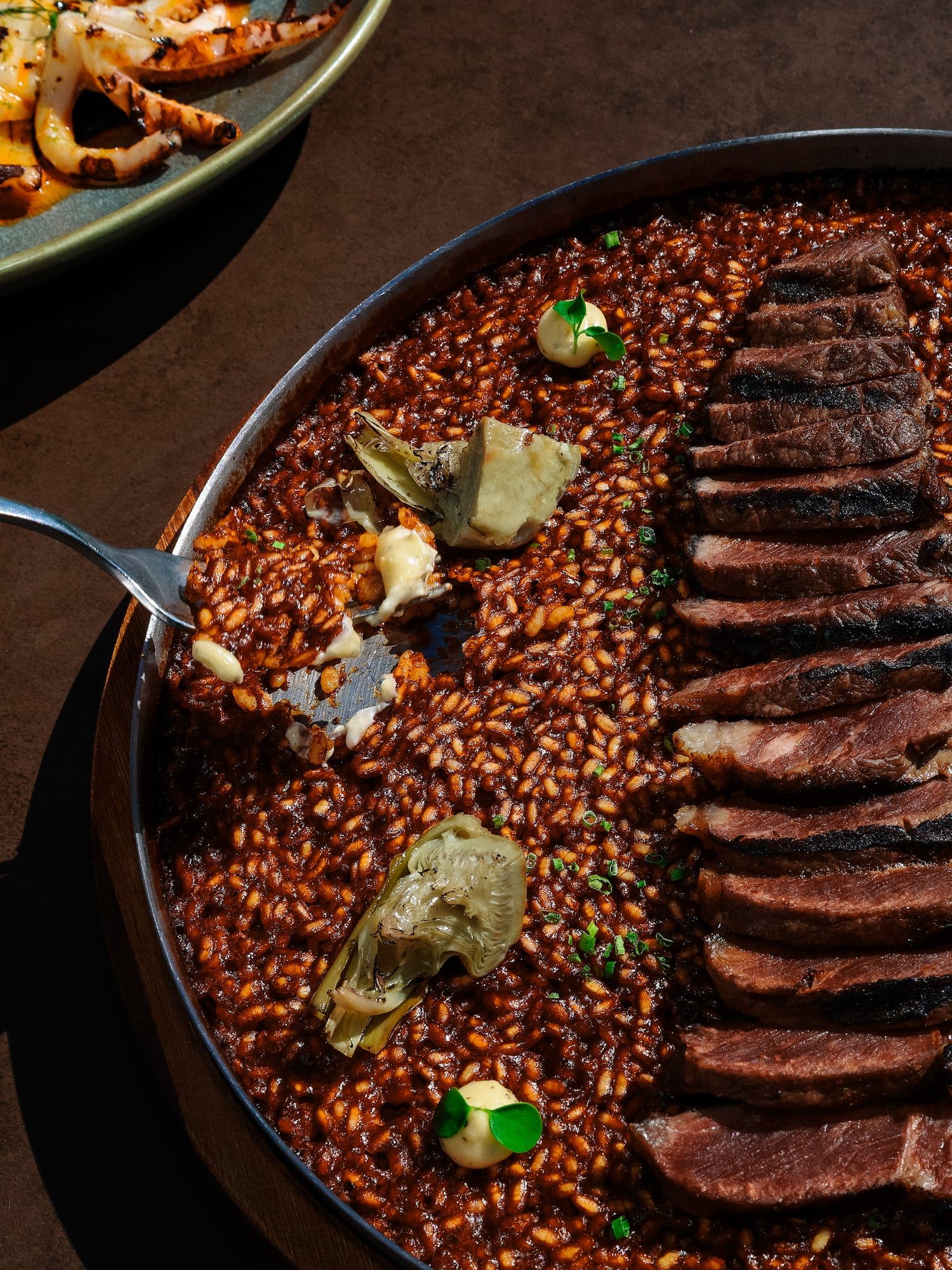 Fork serving dark steak paella with artichokes and grilled calamari.