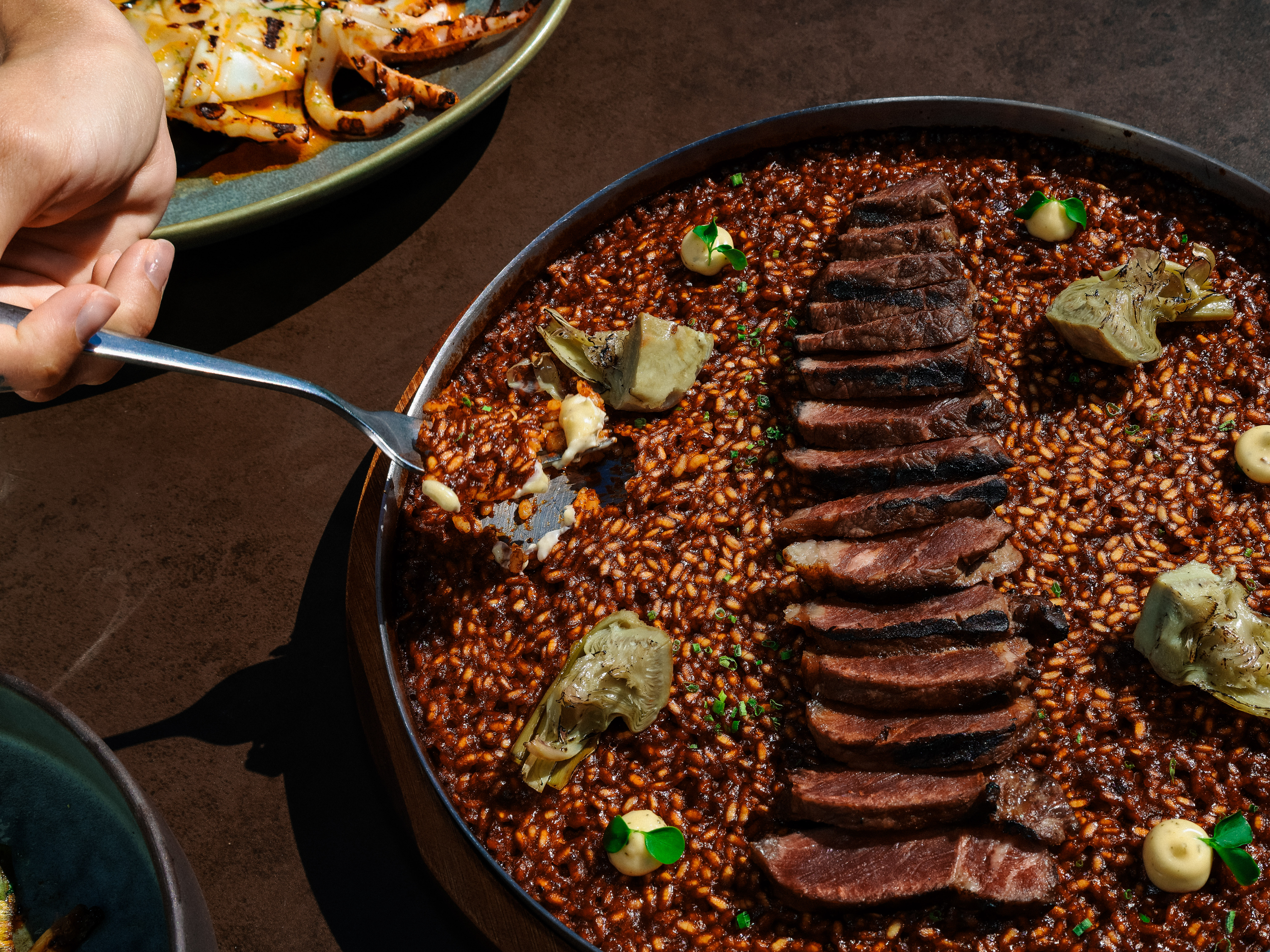 Fork serving dark steak paella with artichokes and grilled calamari.