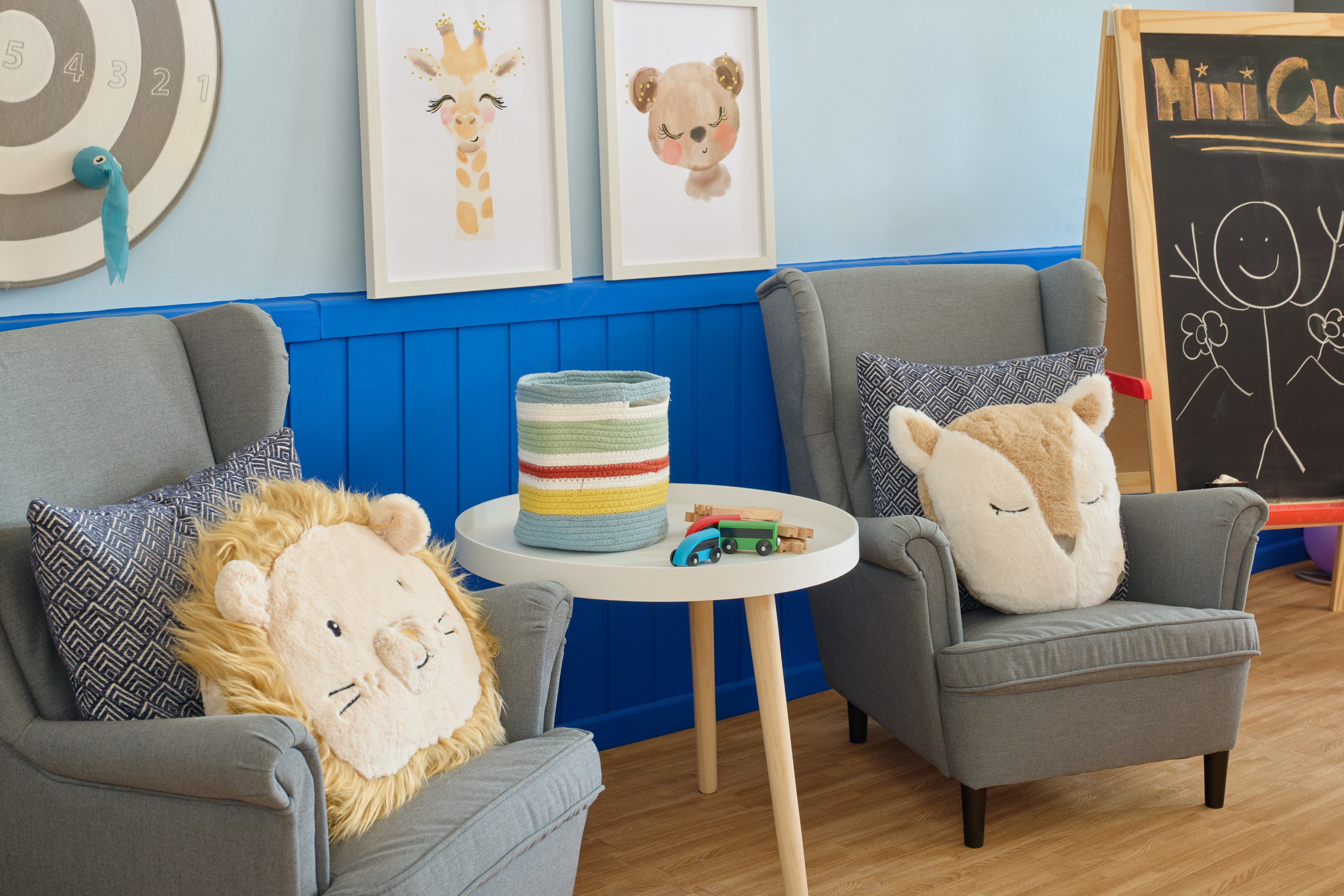Children's room featuring armchairs, animal cushions, toy cars, and framed wall art.