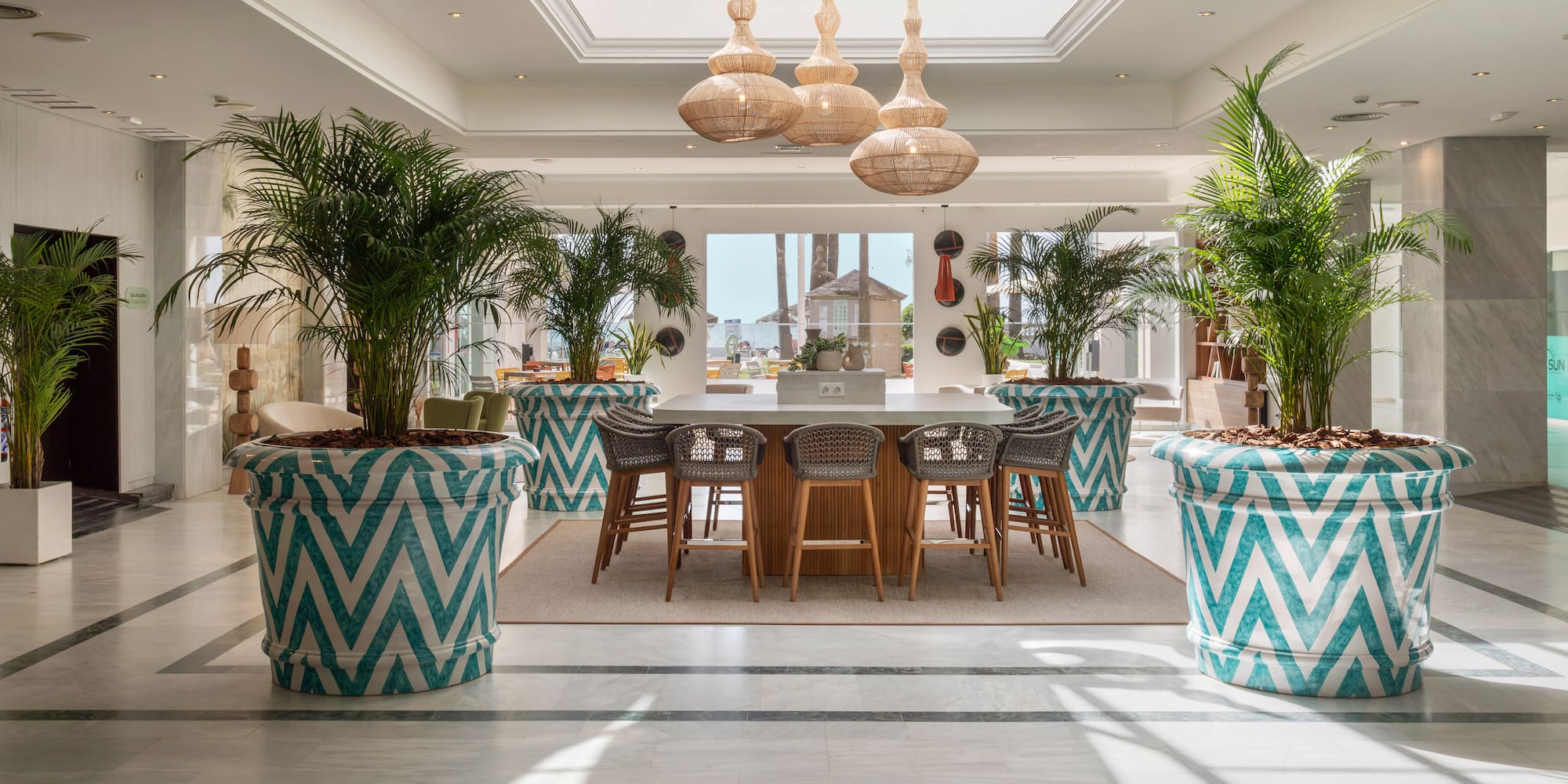 Resort lobby with palm trees in zig-zag planters and a central bar area.