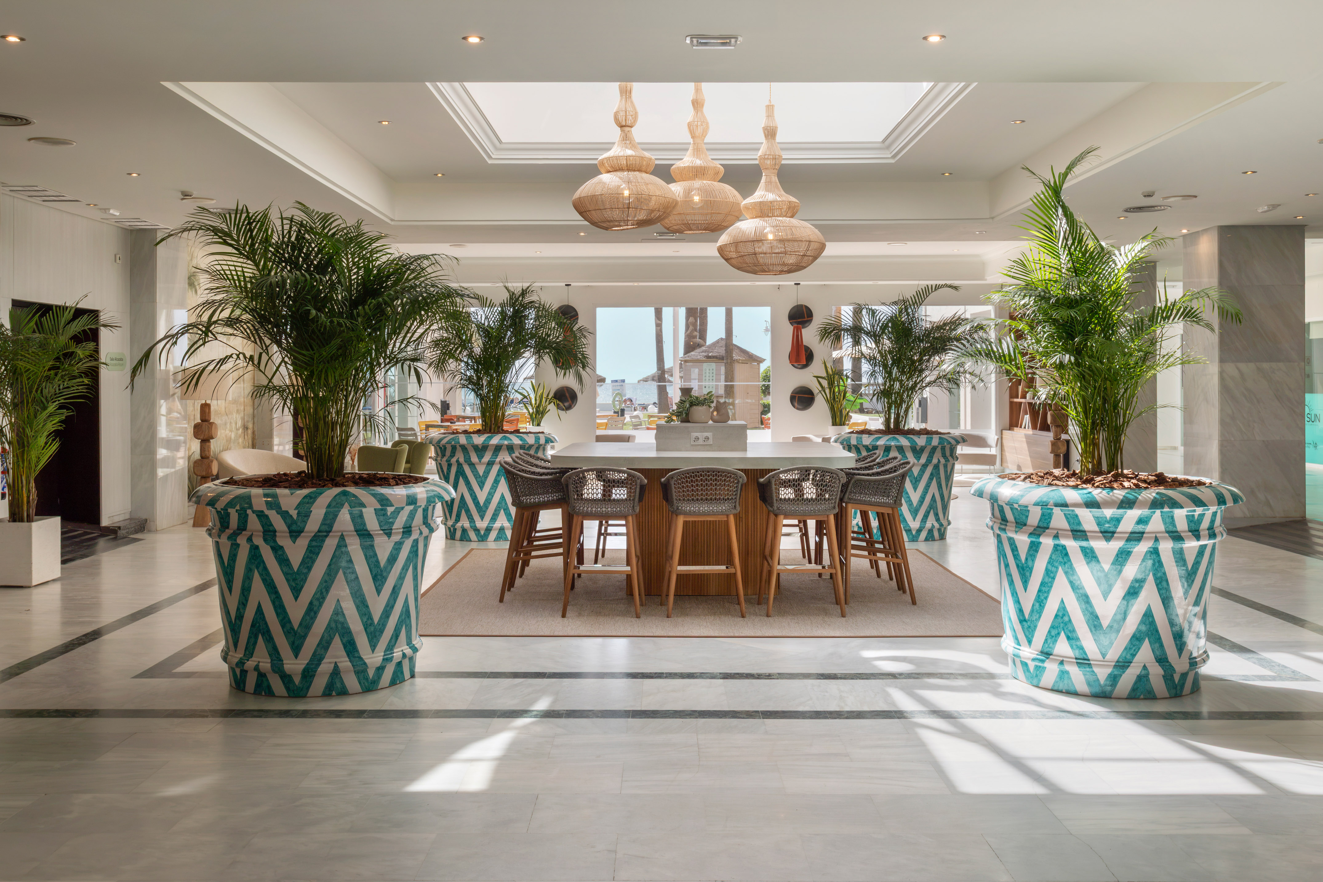 Resort lobby with palm trees in zig-zag planters and a central bar area.