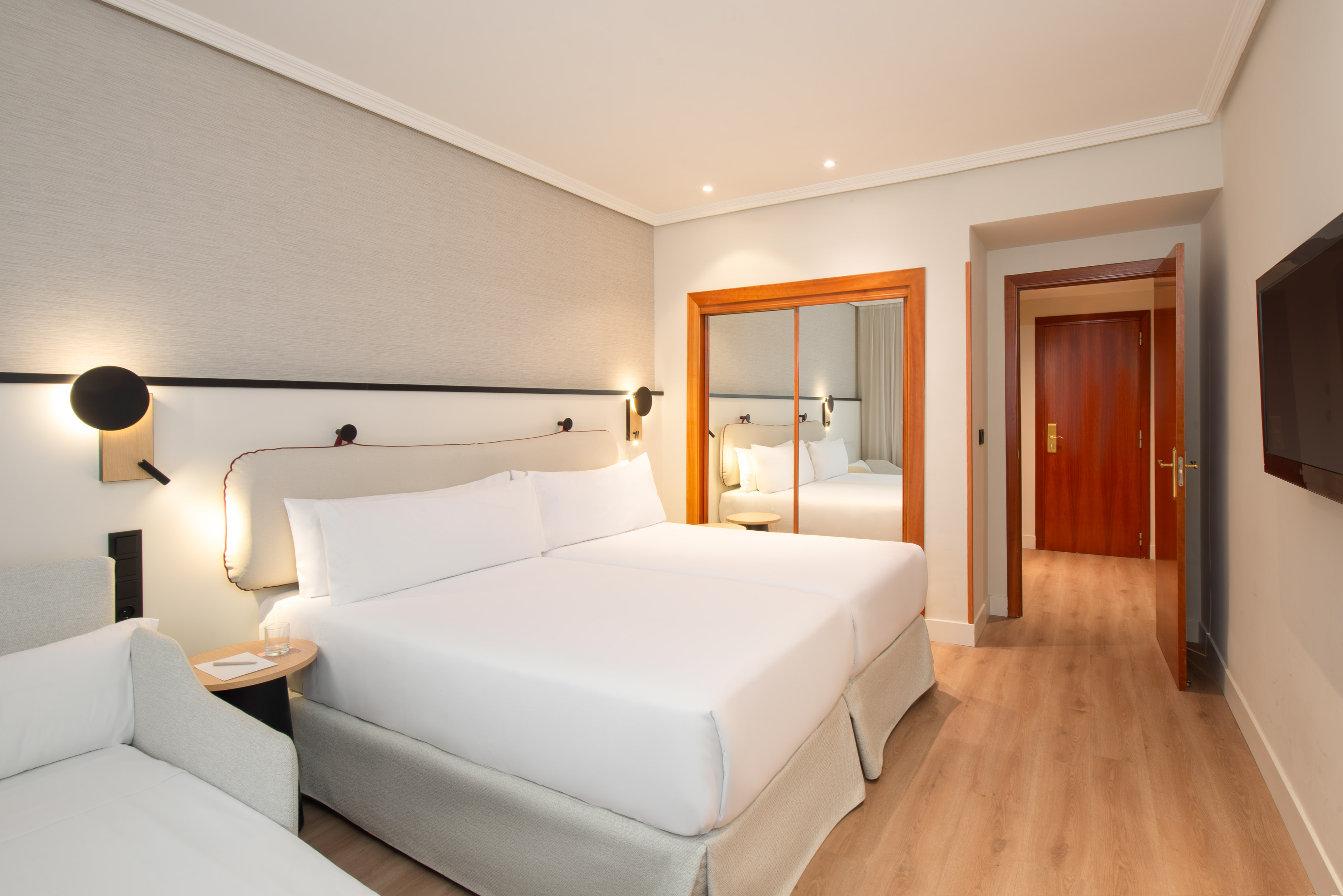 Modern hotel room with two beds, wood flooring, and mirrored wardrobe.