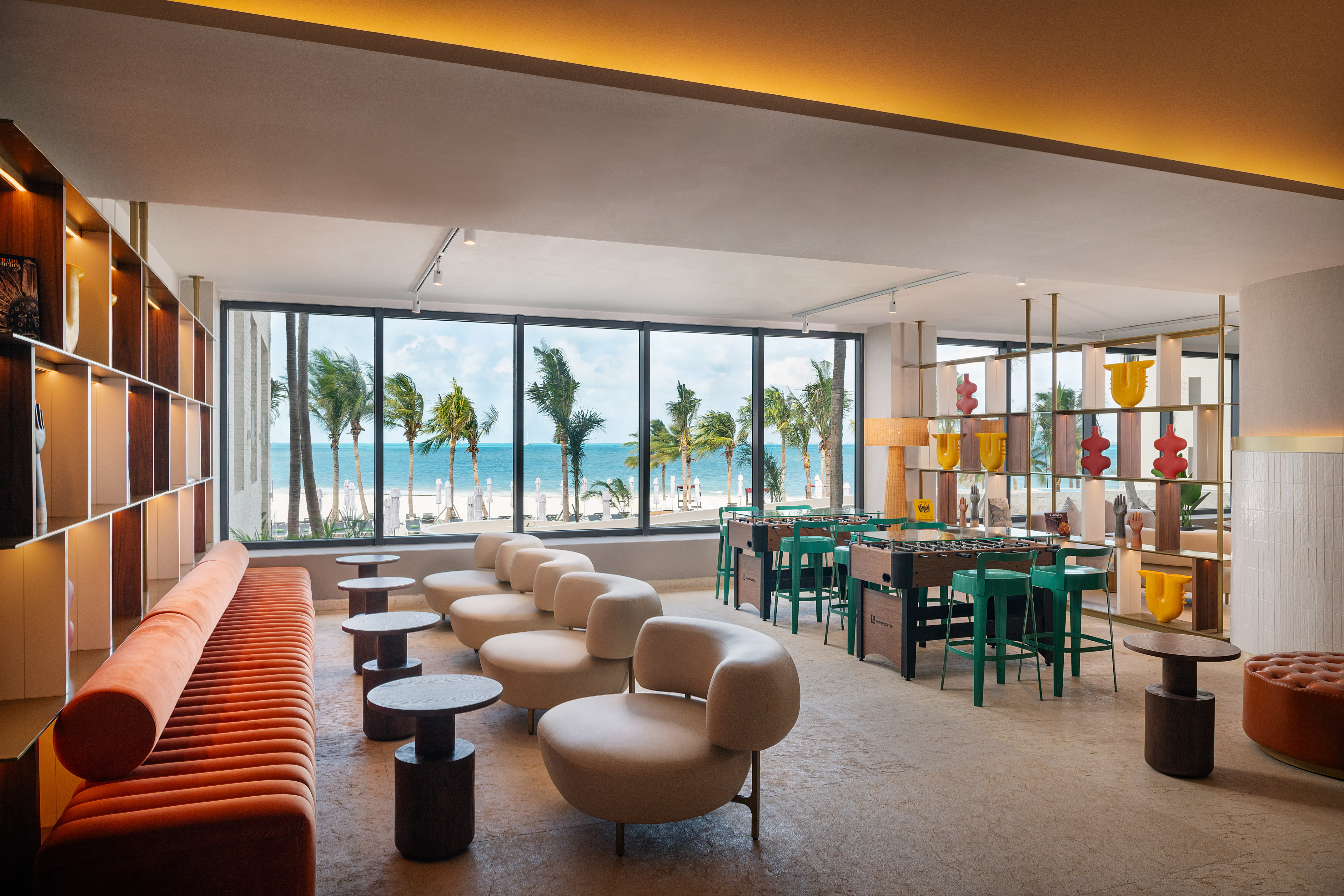 Modern beach resort lounge with ocean view, palm trees, and foosball tables.