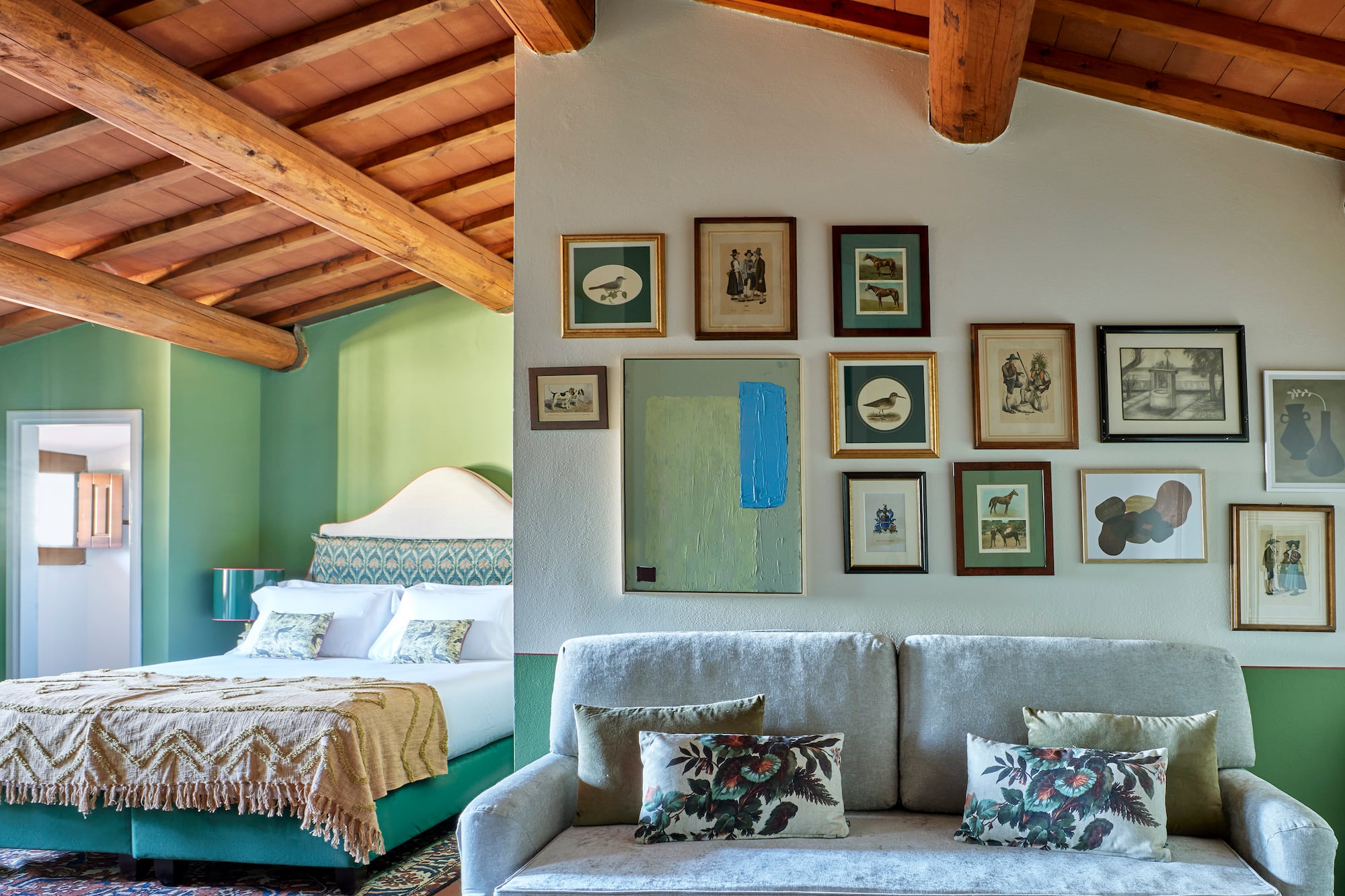 Cozy room with rustic wooden beams, green walls, bed, sofa, and gallery wall.