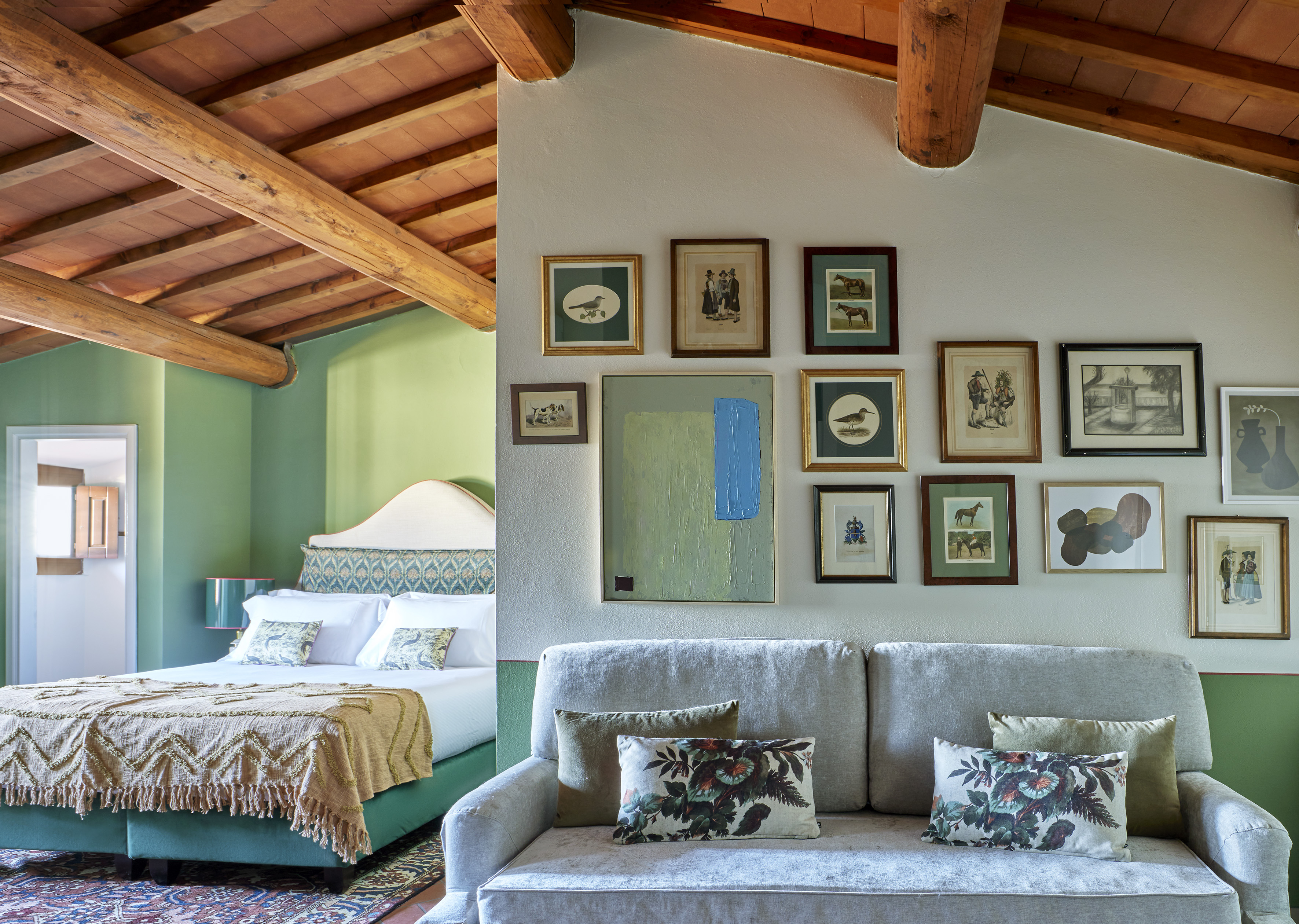 Cozy room with rustic wooden beams, green walls, bed, sofa, and gallery wall.