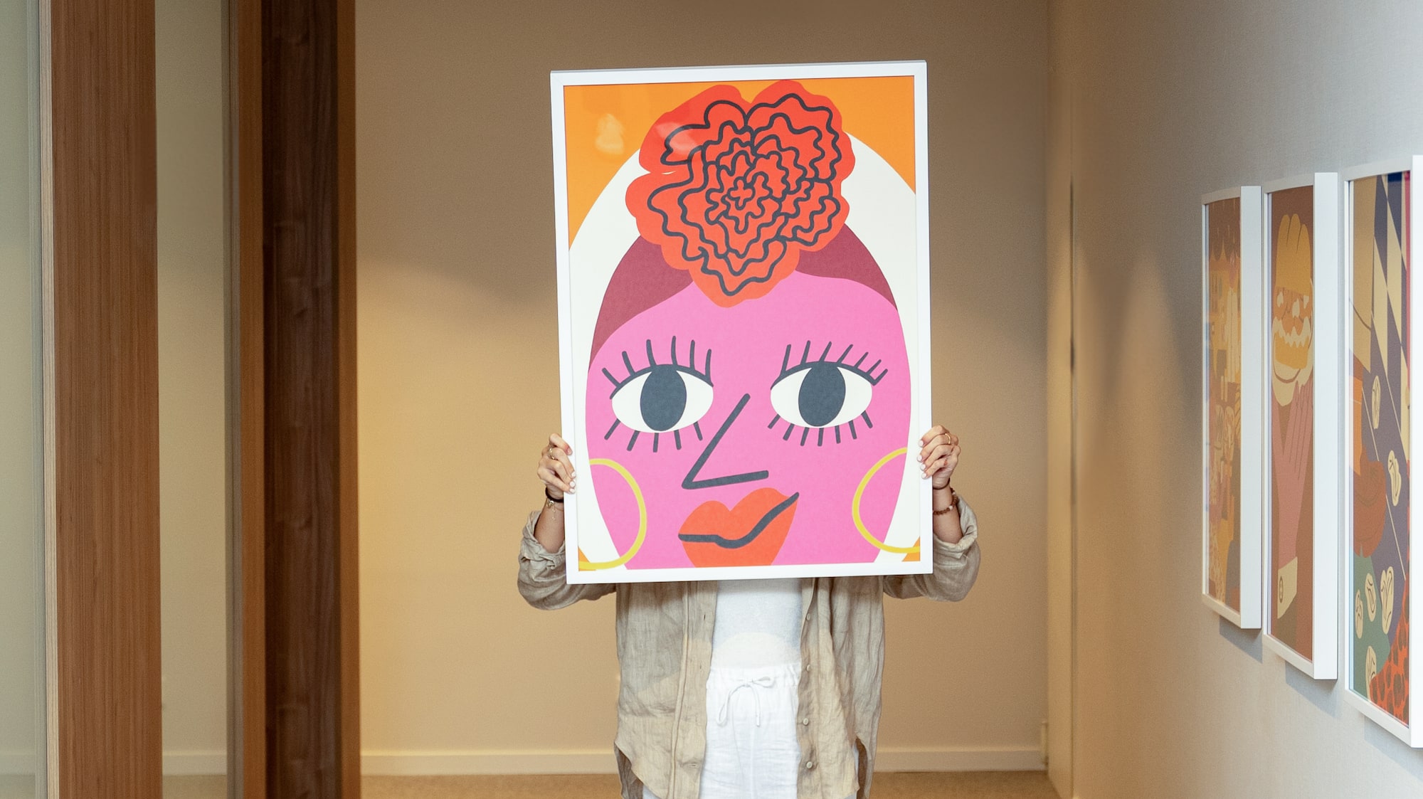 Colorful abstract face art print held by person in modern gallery hallway.
