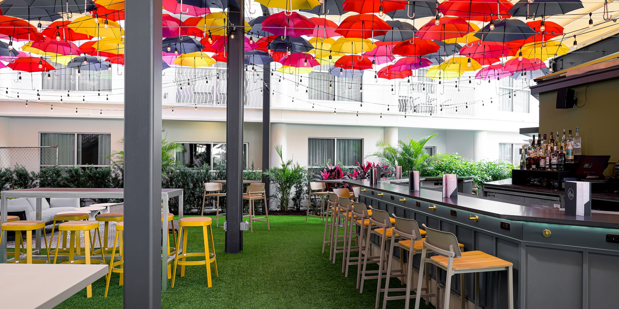 Vibrant outdoor bar with colorful umbrellas, string lights, and green turf.