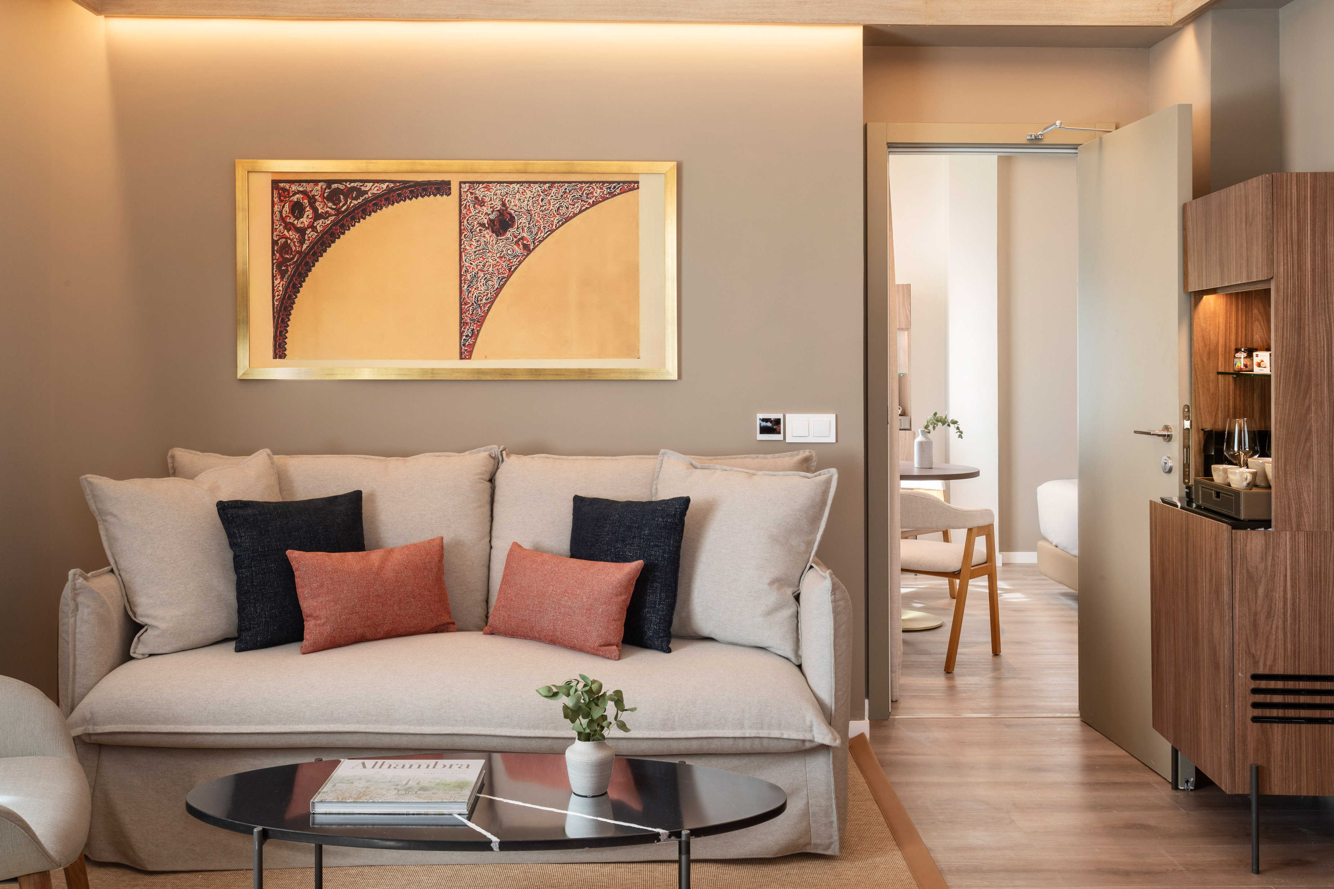 Modern hotel suite living room with sofa, decorative art, and open doorway.
