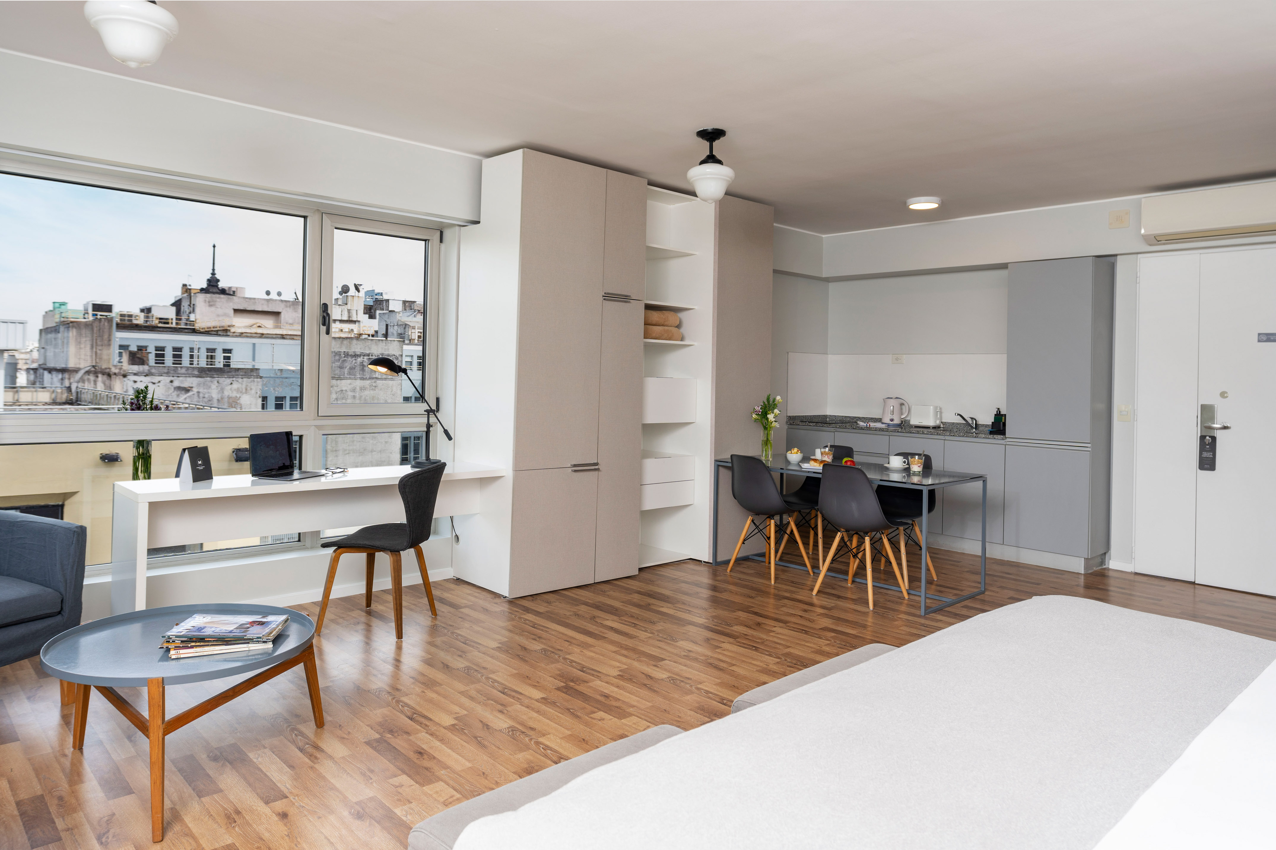 Modern studio apartment with living area, kitchen, desk, and city view.