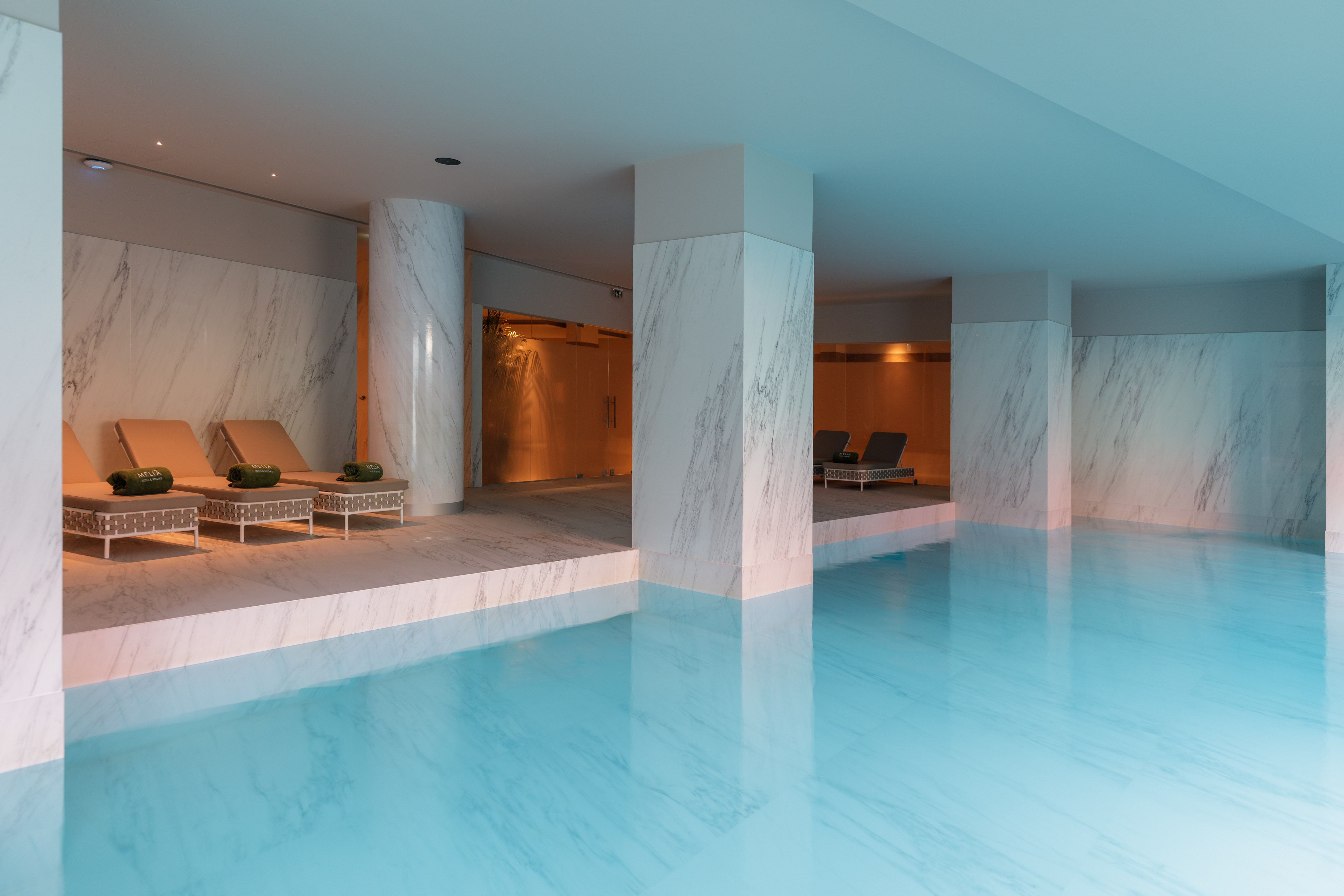 Luxury indoor hotel pool with marble walls, columns, and lounge chairs.