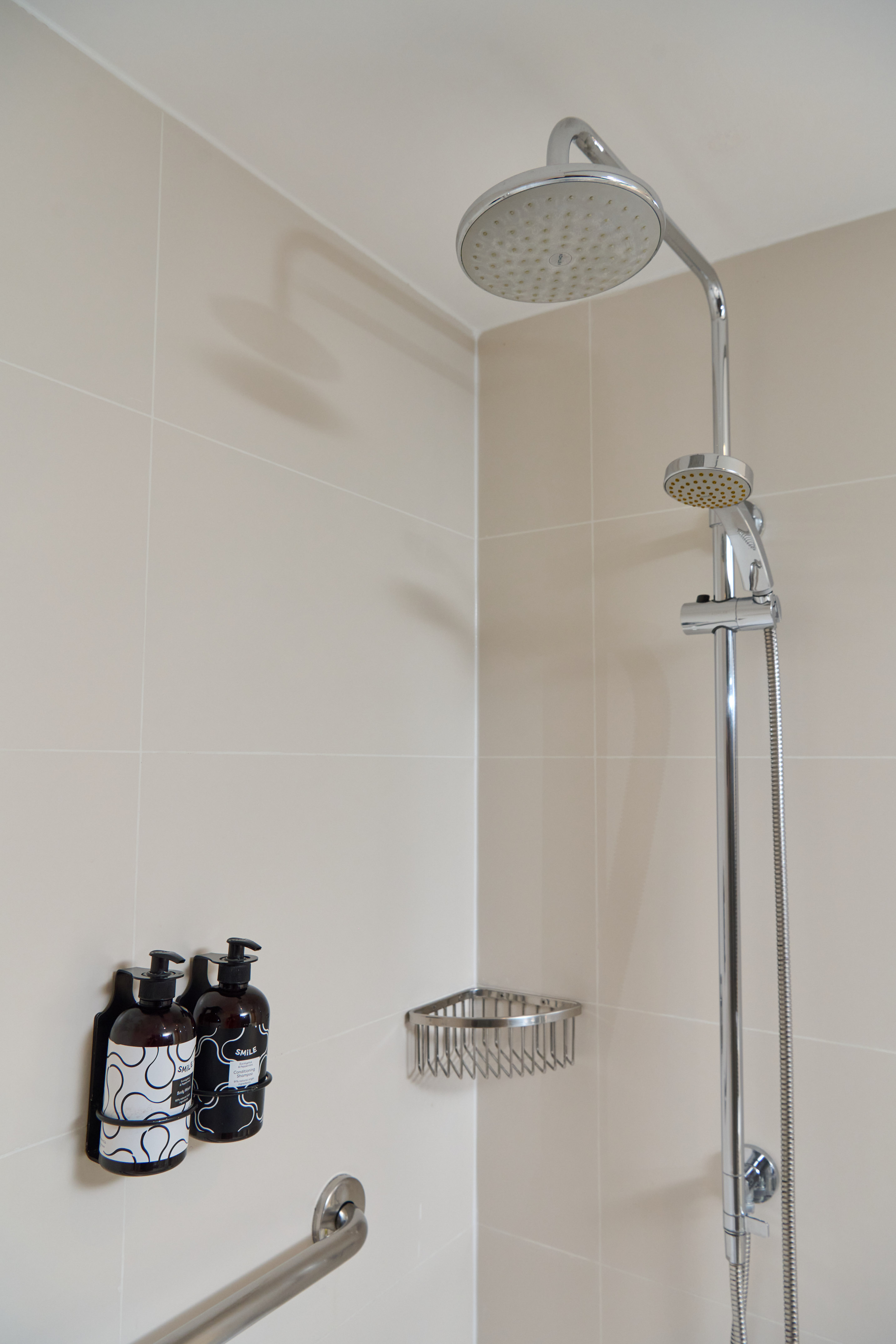 Beige tiled modern shower with rain head, handheld, shampoo/body wash, grab bar.