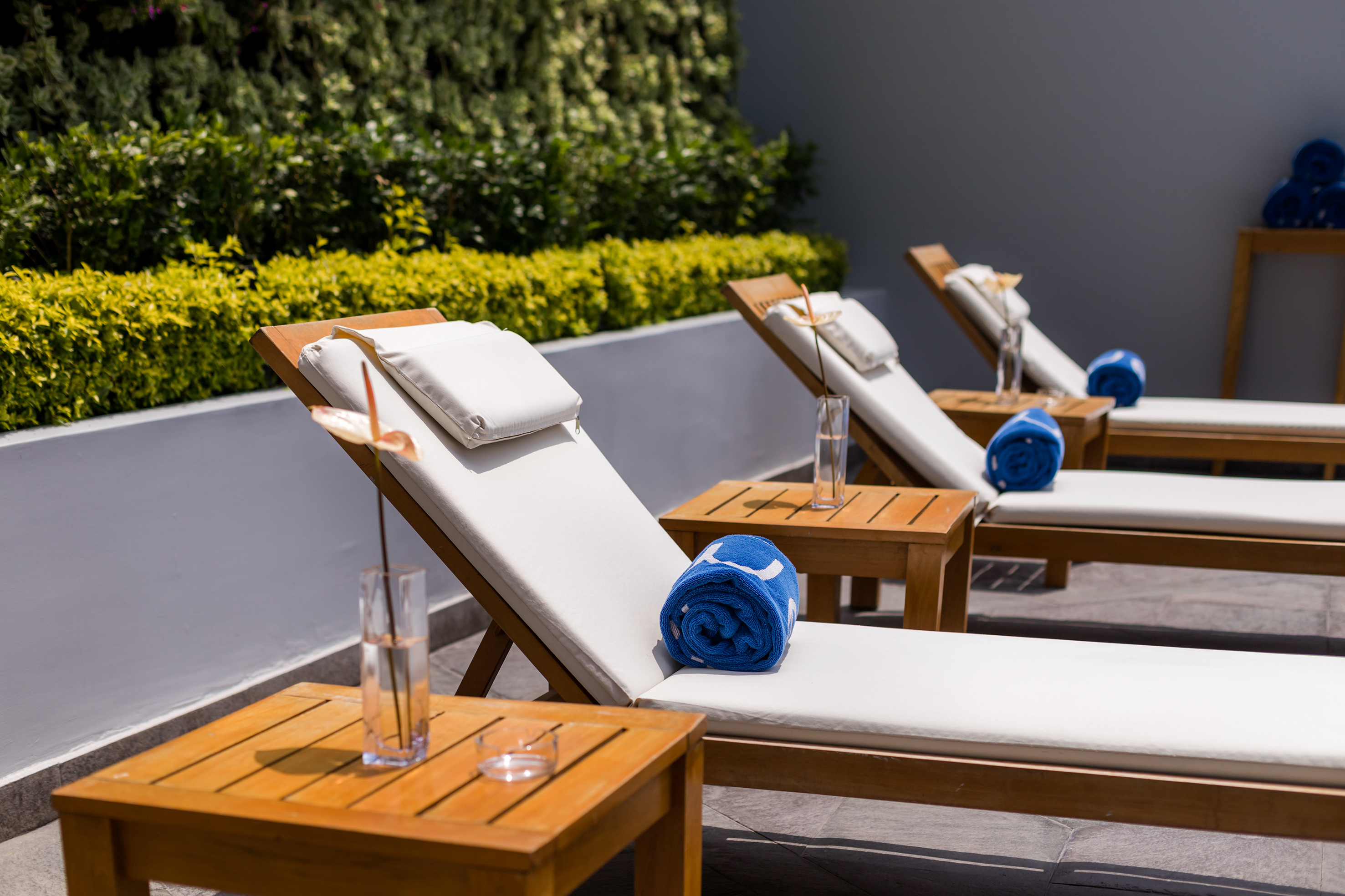 Sunny patio with wooden lounge chairs, white cushions, and blue towels.