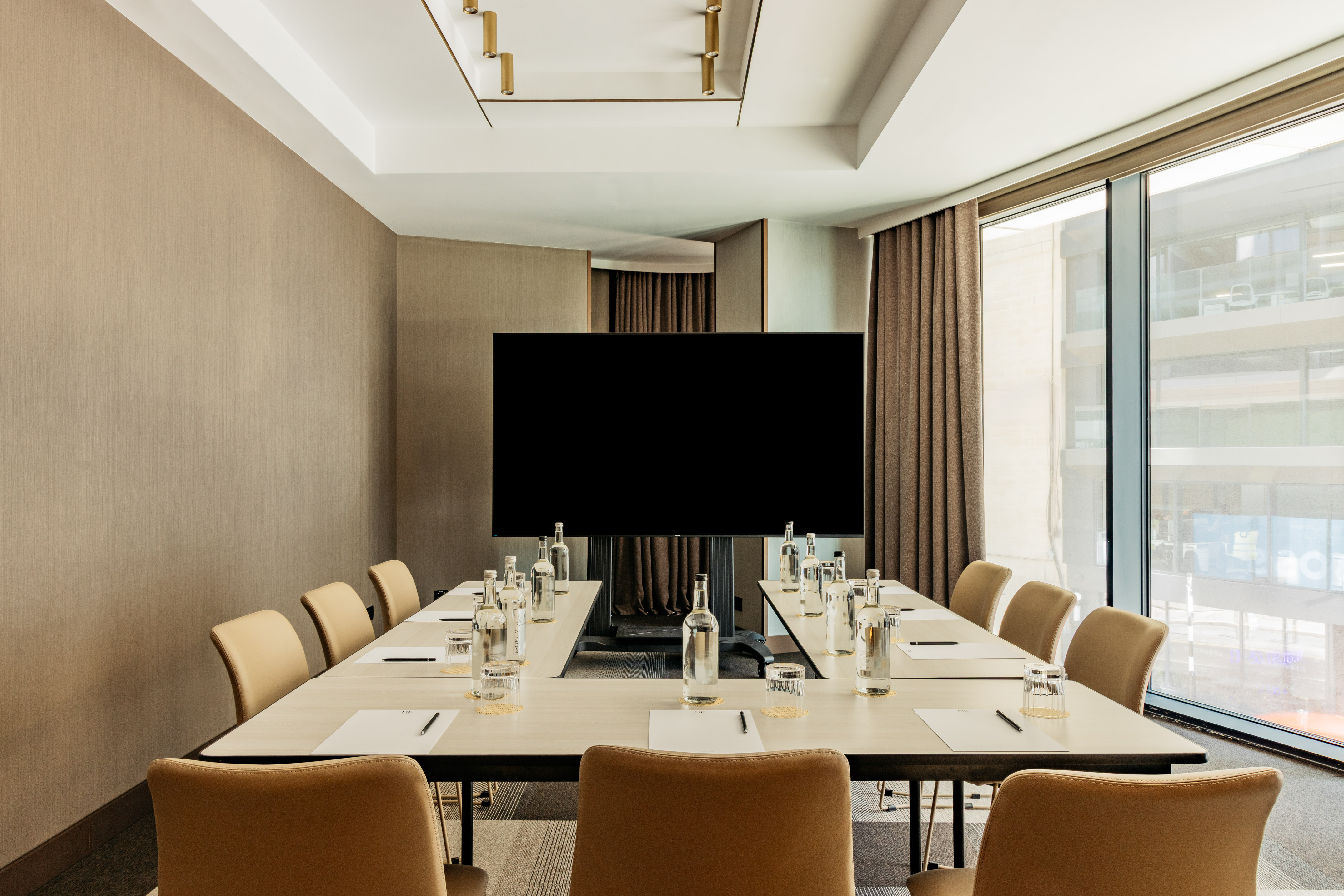 Modern U-shaped conference room with large display screen and natural light.