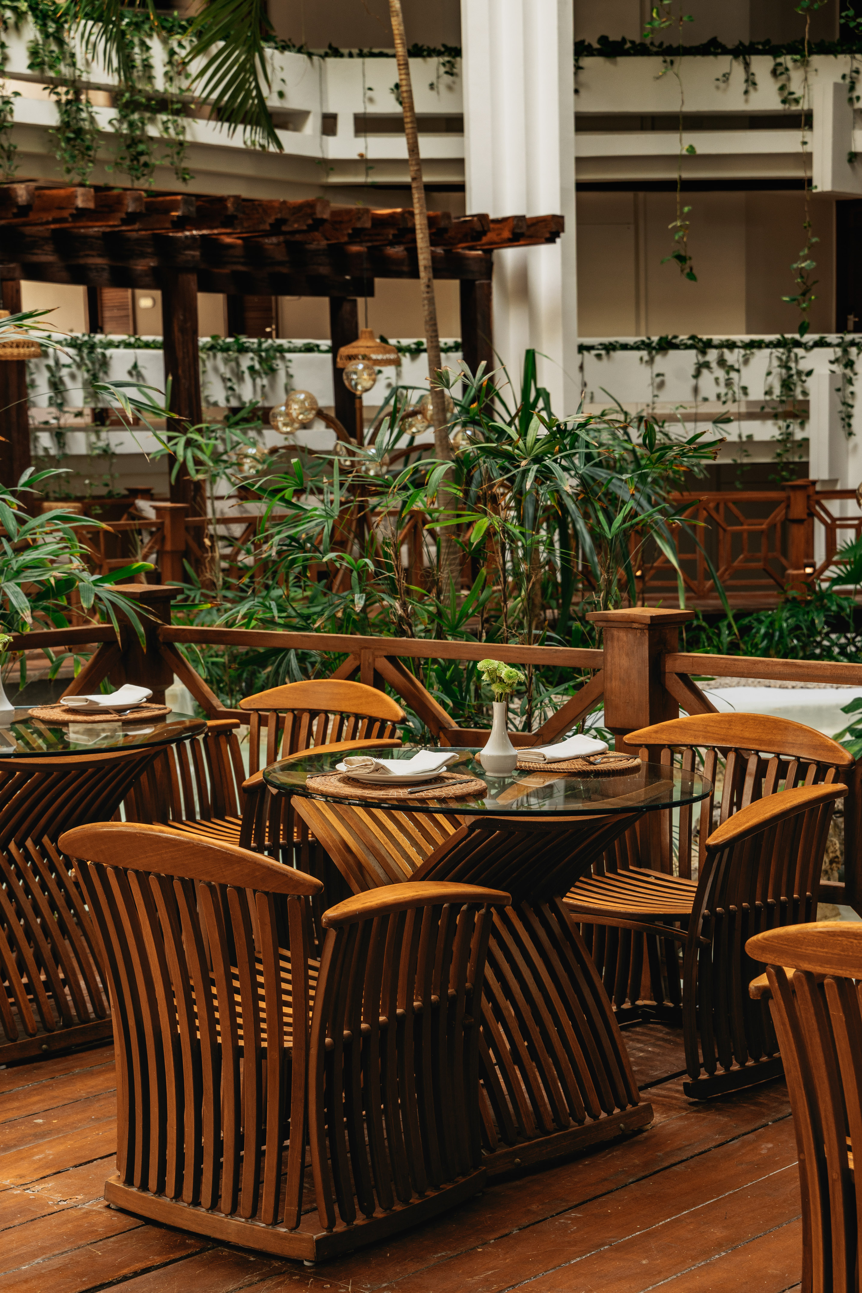 Lush tropical restaurant patio with wooden tables, slatted chairs, and greenery.