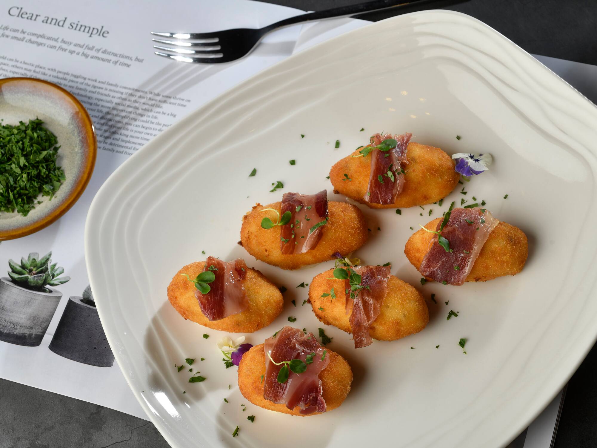 food on a plate accompanied by a fork and a cup of sauce