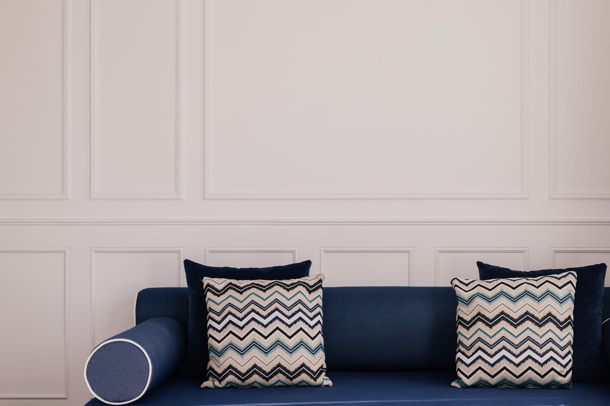 Blue sofa, zigzag pillows, gold coffee tables against white paneled wall.