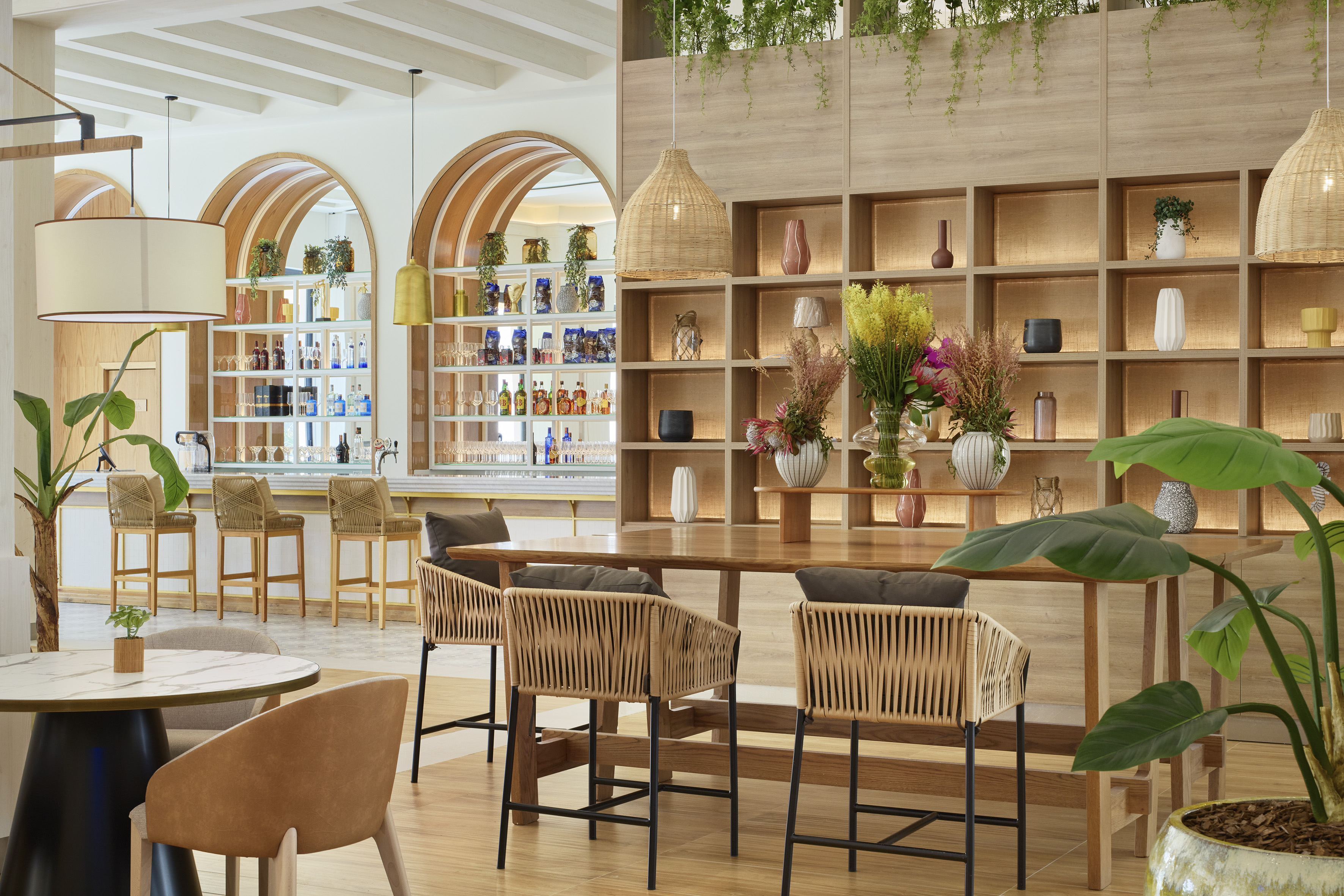 Modern bar lounge with wood shelves, rattan stools, and lush plants.