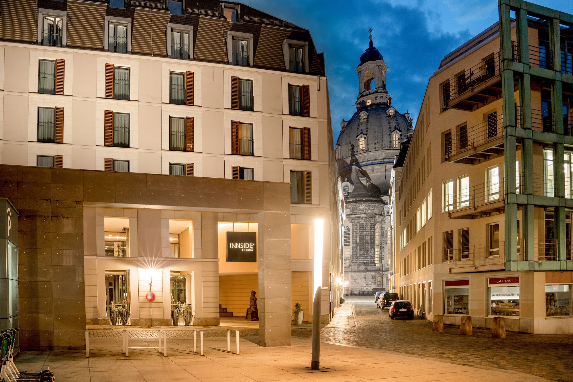 Innside by Meliá Dresden hotel façade at dusk, with illuminated Frauenkirche dome.