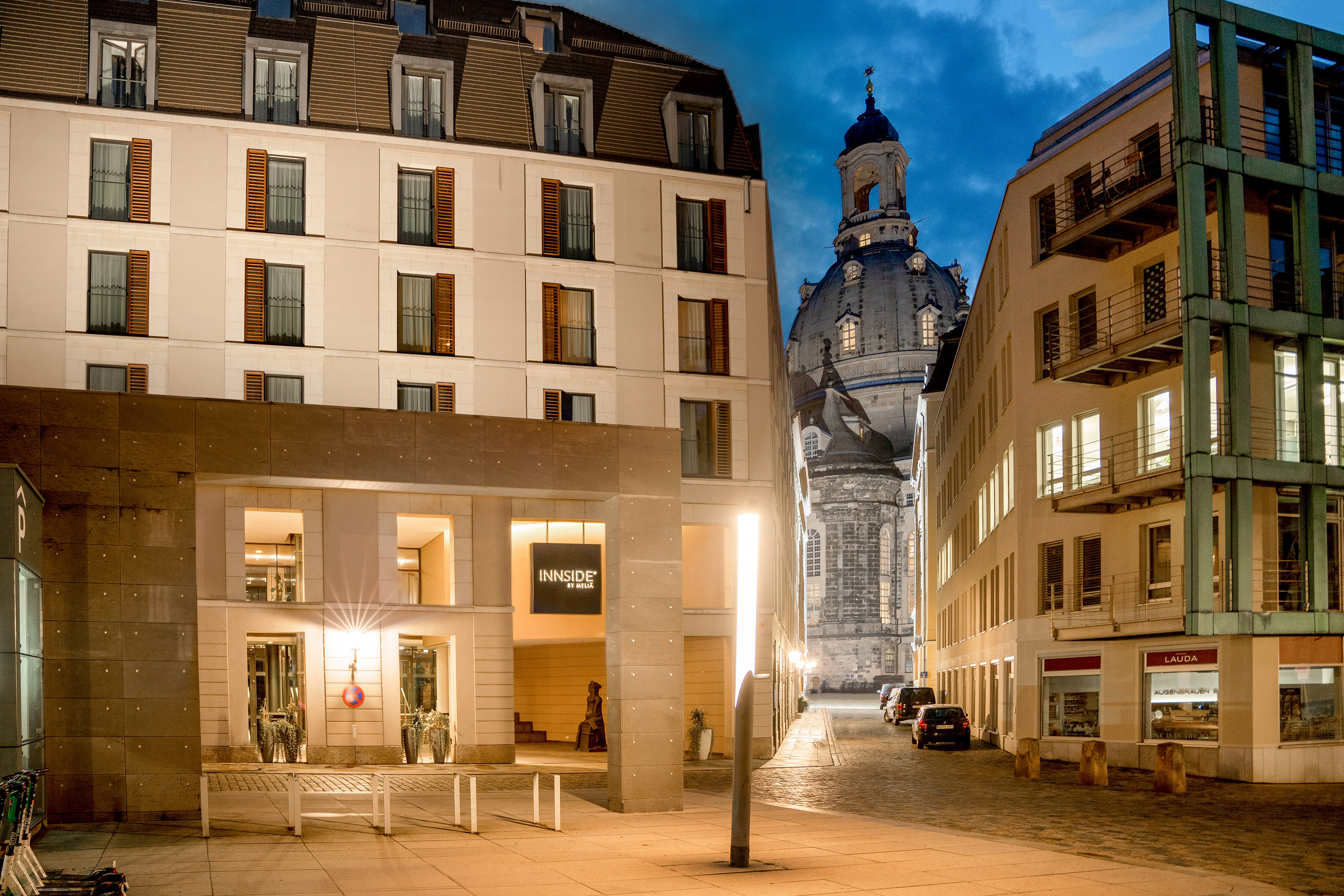 Innside by Meliá Dresden hotel façade at dusk, with illuminated Frauenkirche dome.