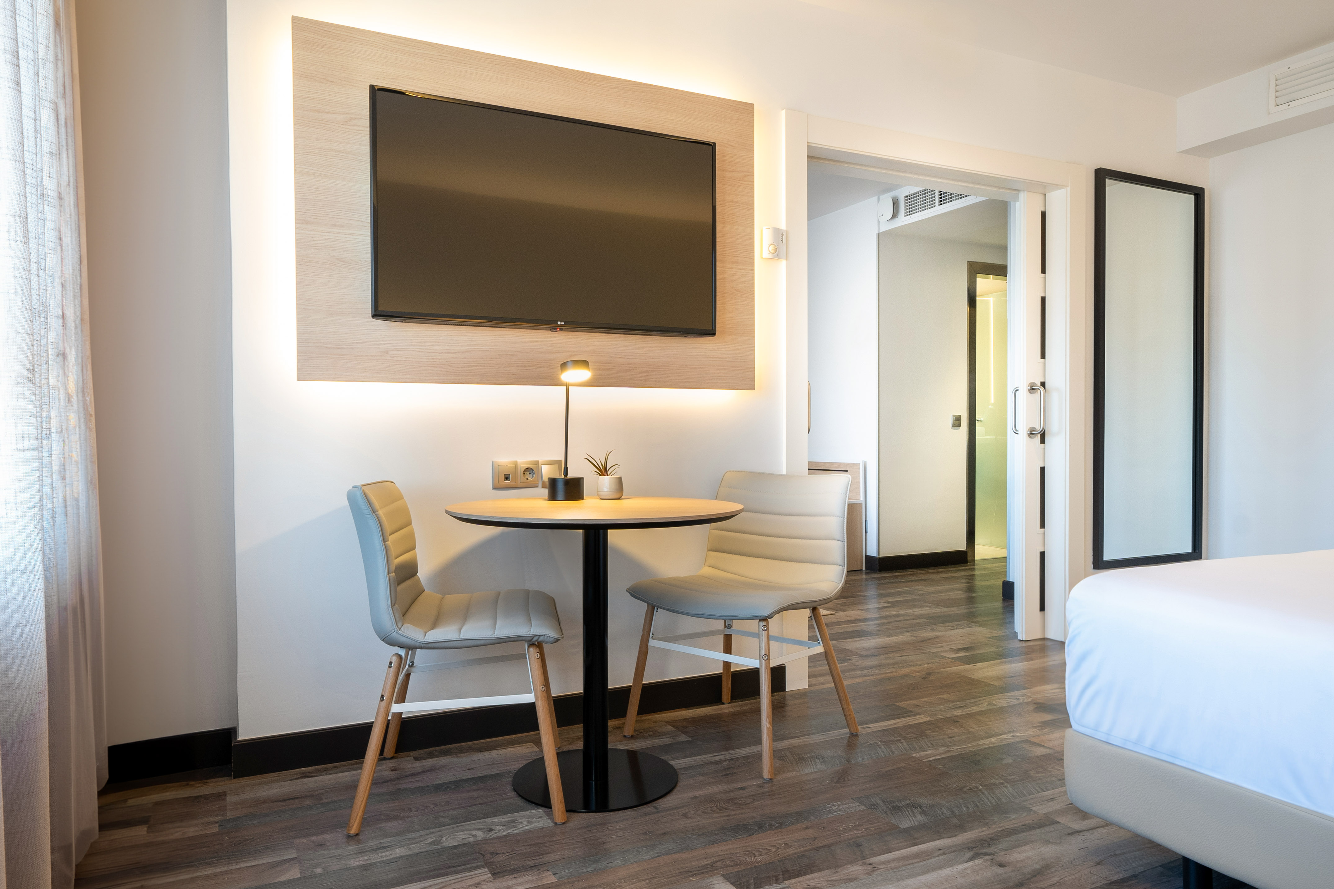 Contemporary hotel suite living area with TV, small table, two chairs.