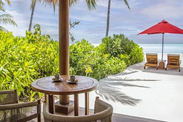 a table and chairs on a patio with a red umbrella and palm trees