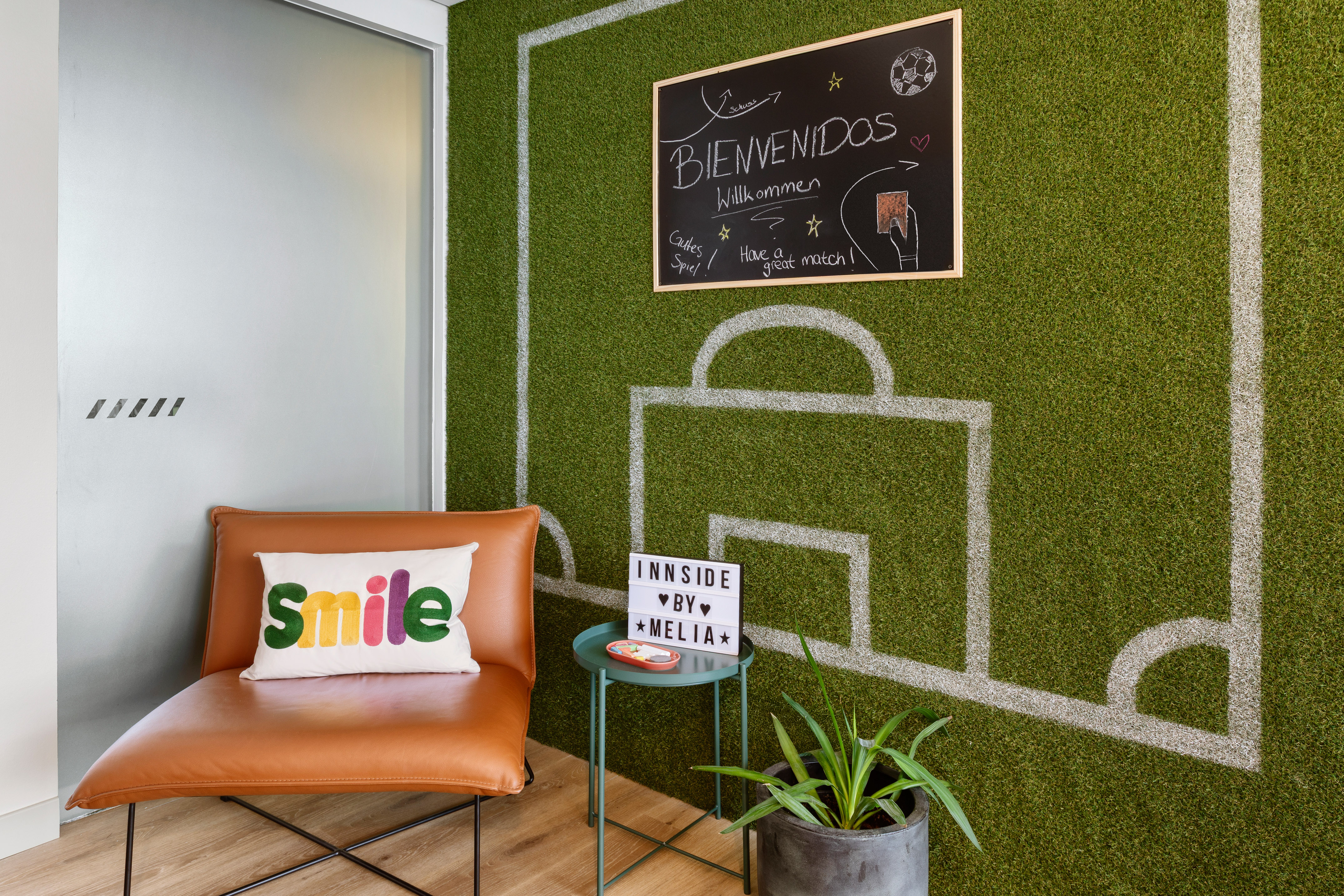 INNSiDE Meliá hotel lobby, soccer grass wall, welcome sign, brown armchair.