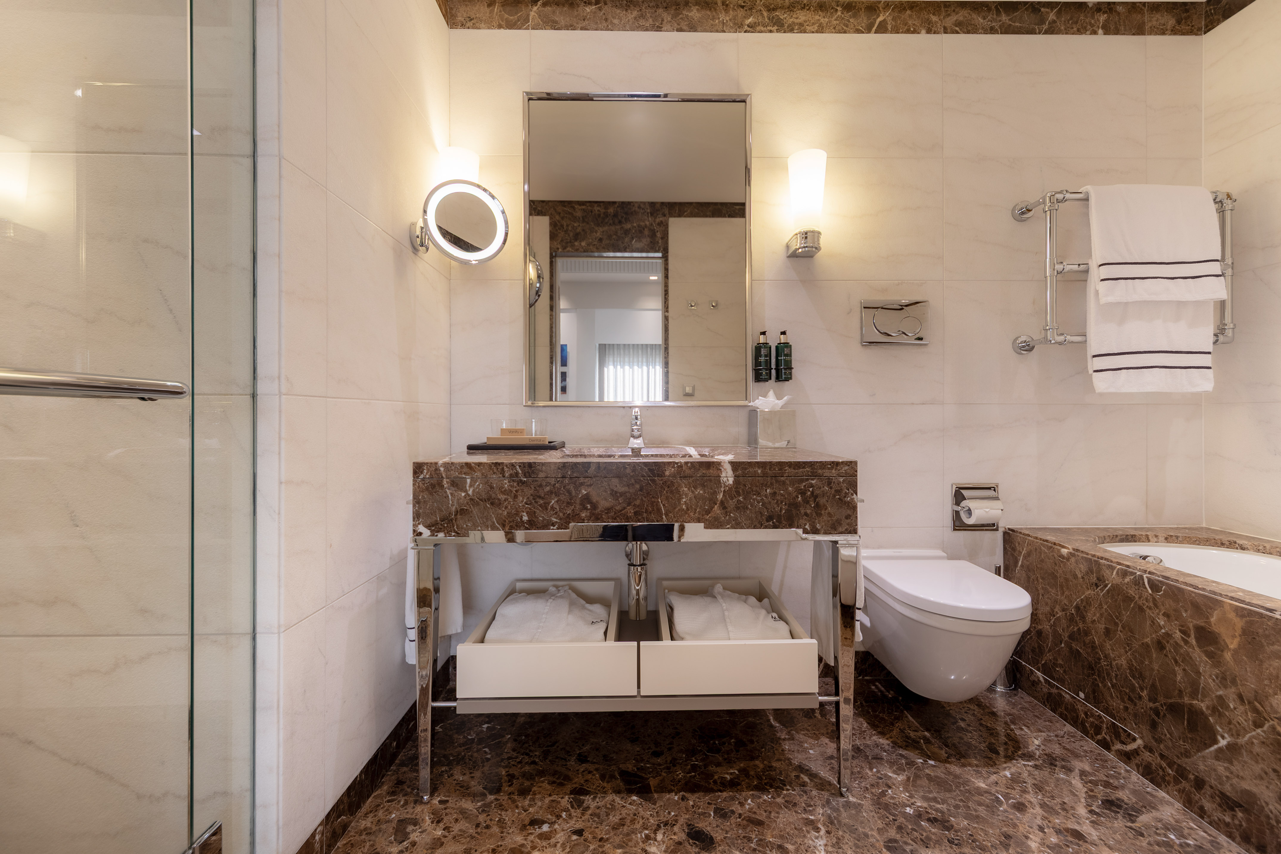 Luxury hotel bathroom with brown marble vanity, mirror, toilet, bathtub, and shower.