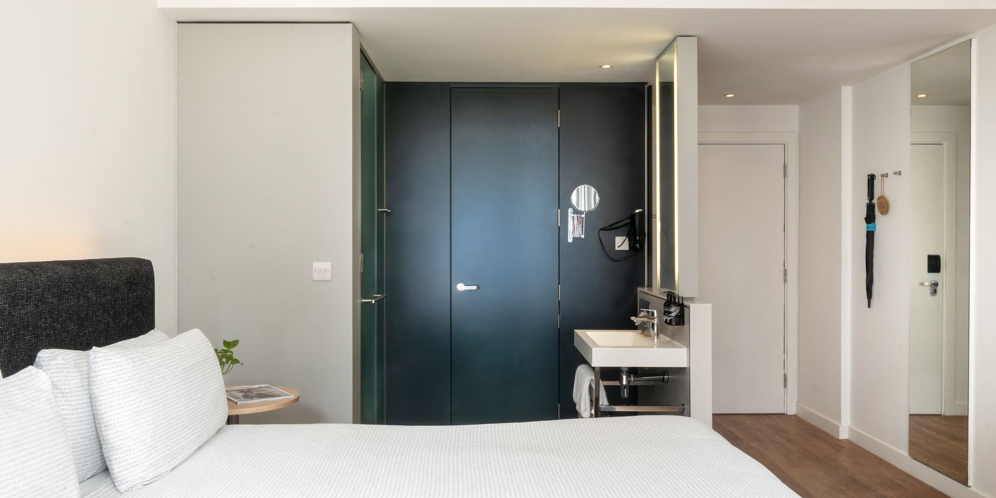 Minimalist hotel room with white bed, integrated vanity, and dark modern doors.